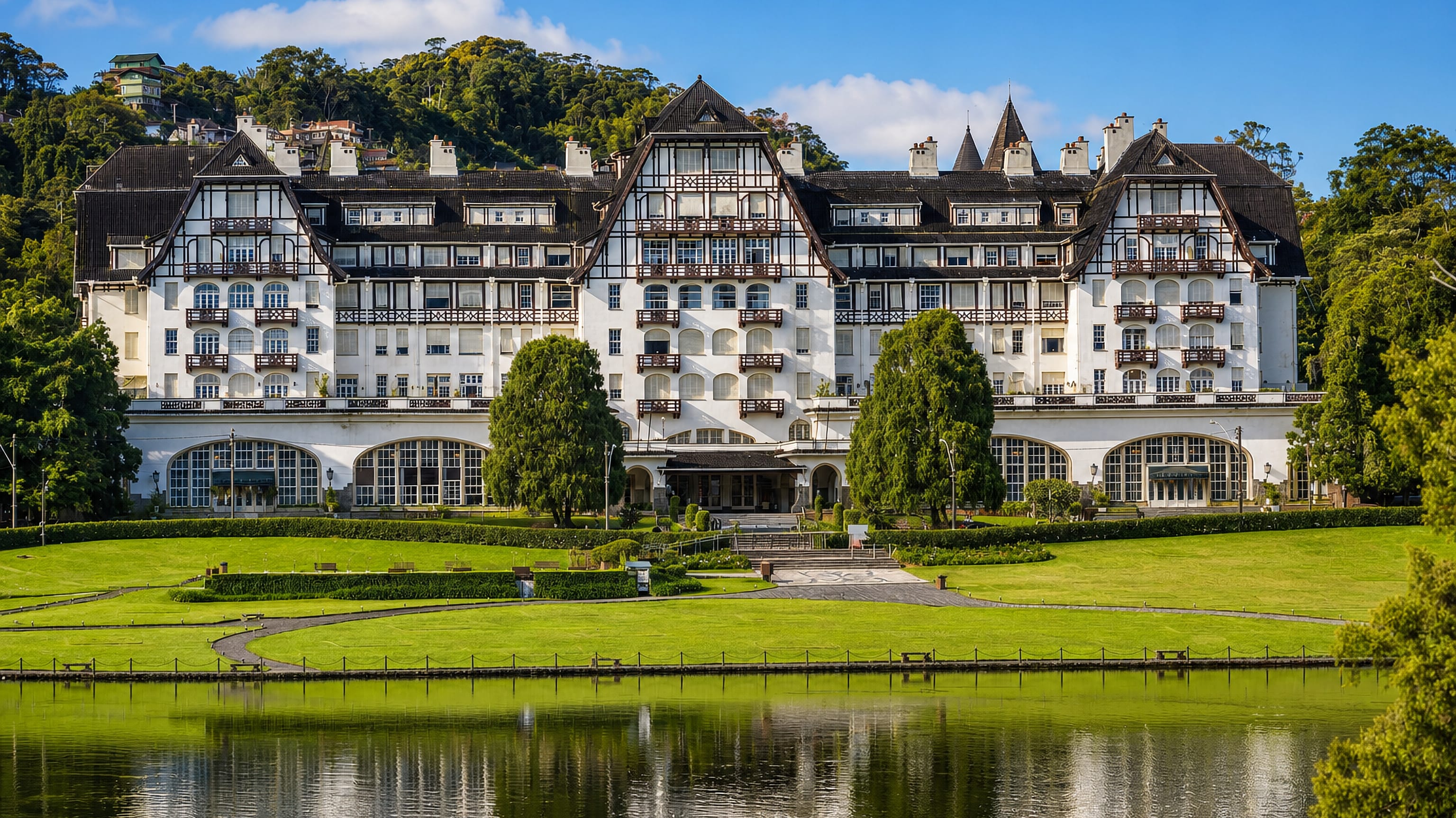 Palacio Quitandinha in Petropolis, Brazil, its half-timbered facade mirrored in the lake below forested hills.