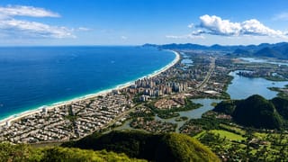 Aerial view of Rio de Janeiro's long curving beach, coastal lagoons and green mountains meeting the Atlantic.