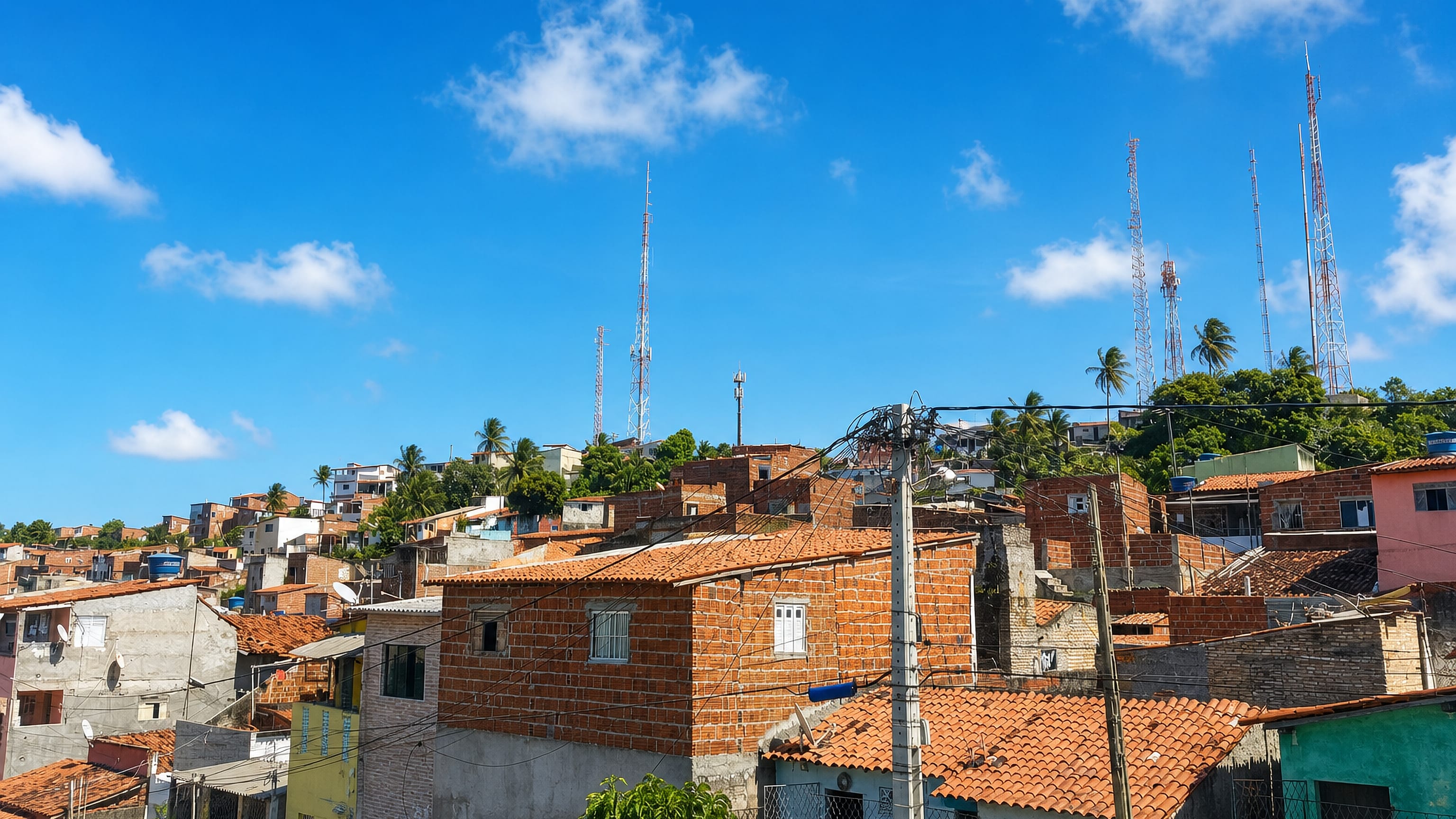 Brick and tile-roofed houses climbing the hillside of Mãe Luiza in Natal, with radio masts and palms.