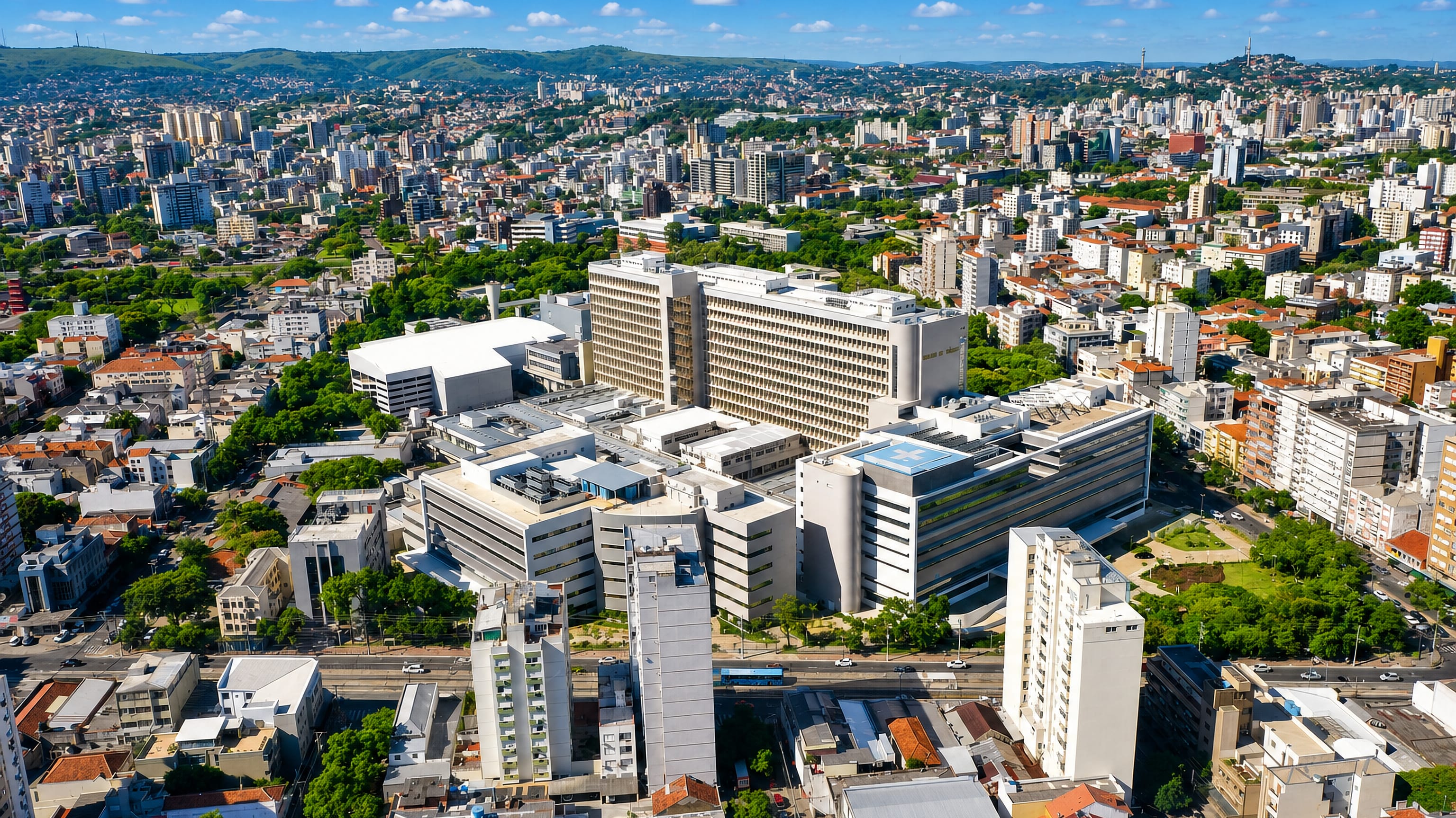 Aerial view of Porto Alegre's dense central district around the Hospital de Clínicas, with green hills beyond