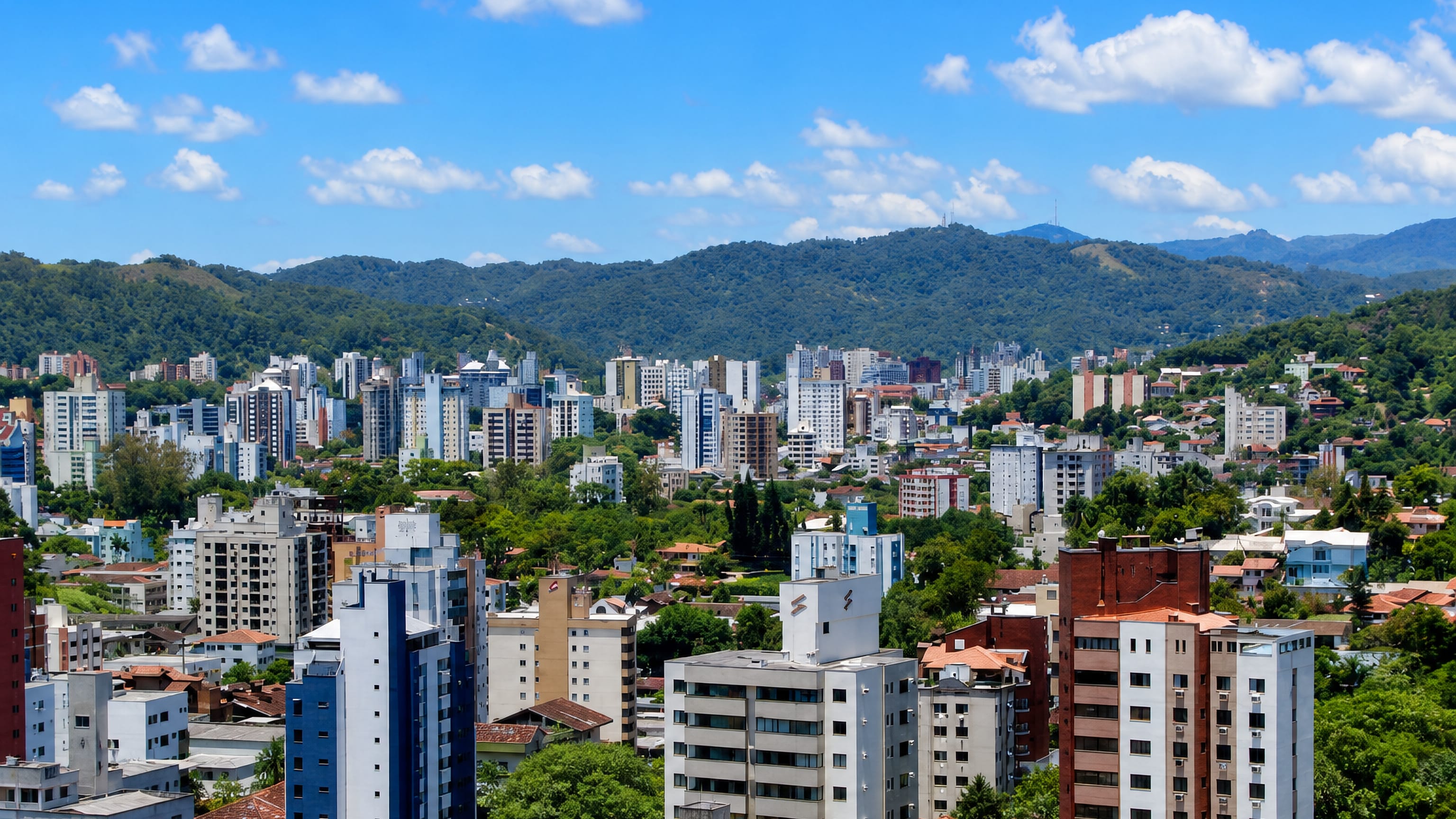 Apartment towers and tile-roofed houses fill Blumenau's green valley in Santa Catarina, Brazil, below forested hills.