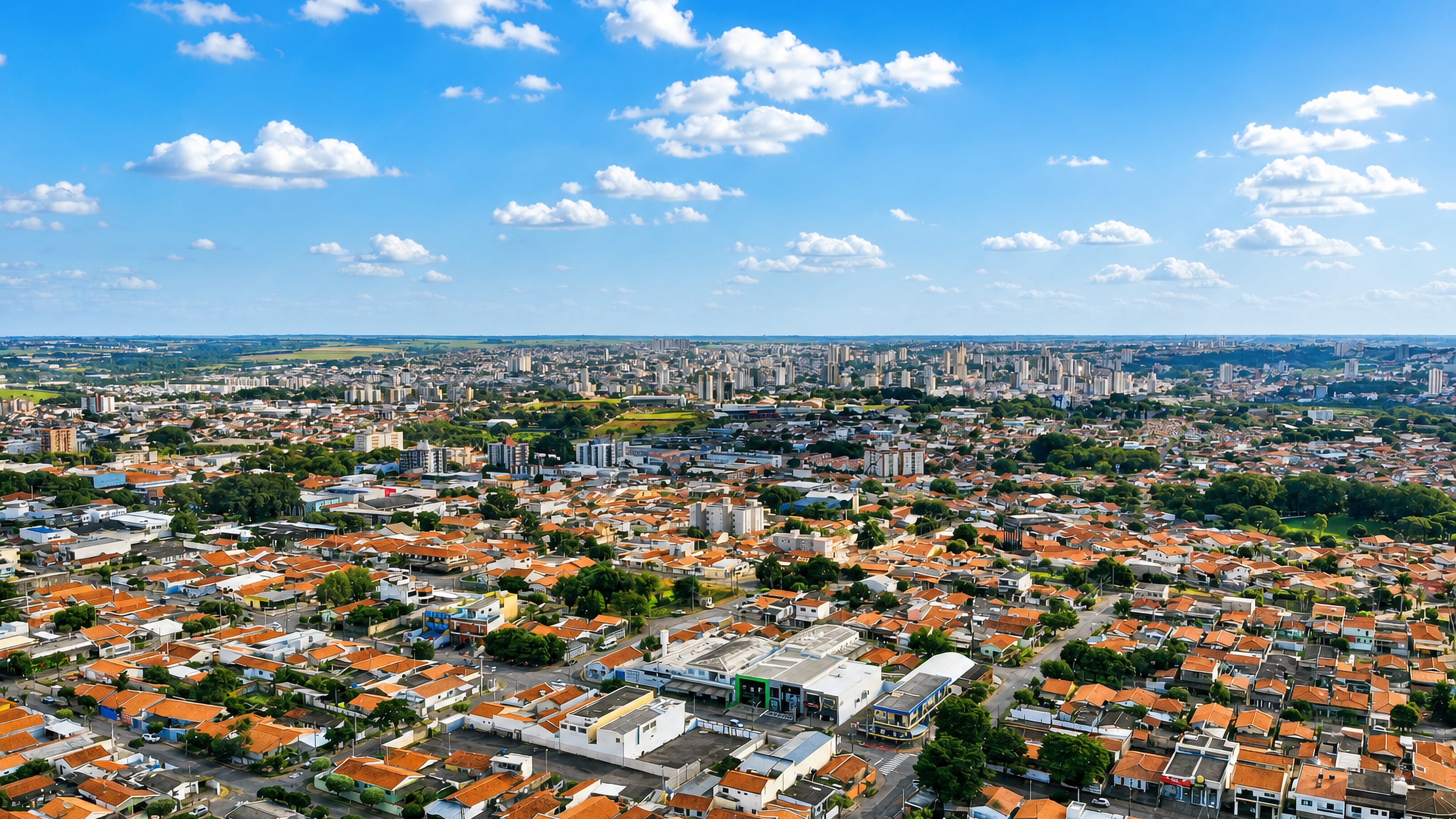 Aerial view of Americana, Brazil, with red-tiled suburban rooftops stretching to a distant mid-rise skyline.