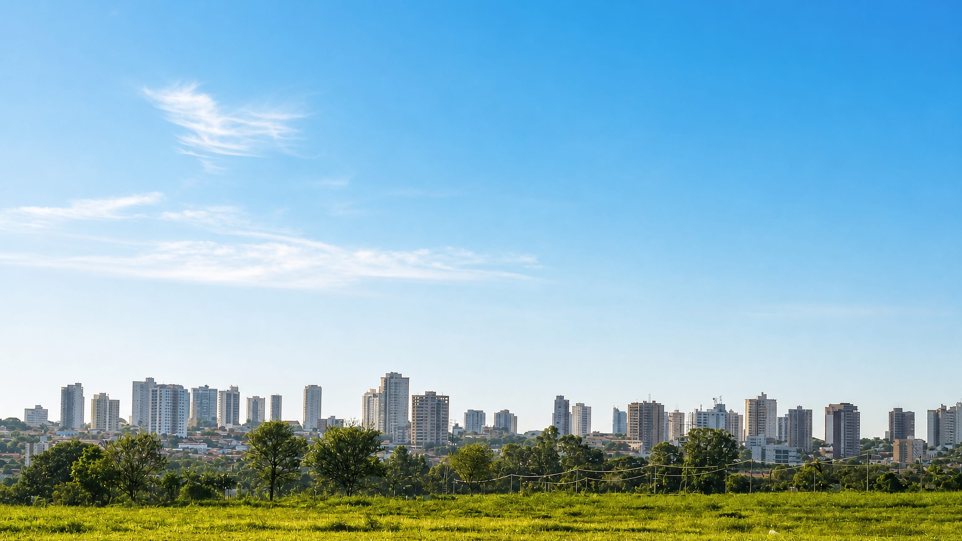 Araçatuba's apartment-tower skyline on the Sao Paulo plateau seen across an open green field.