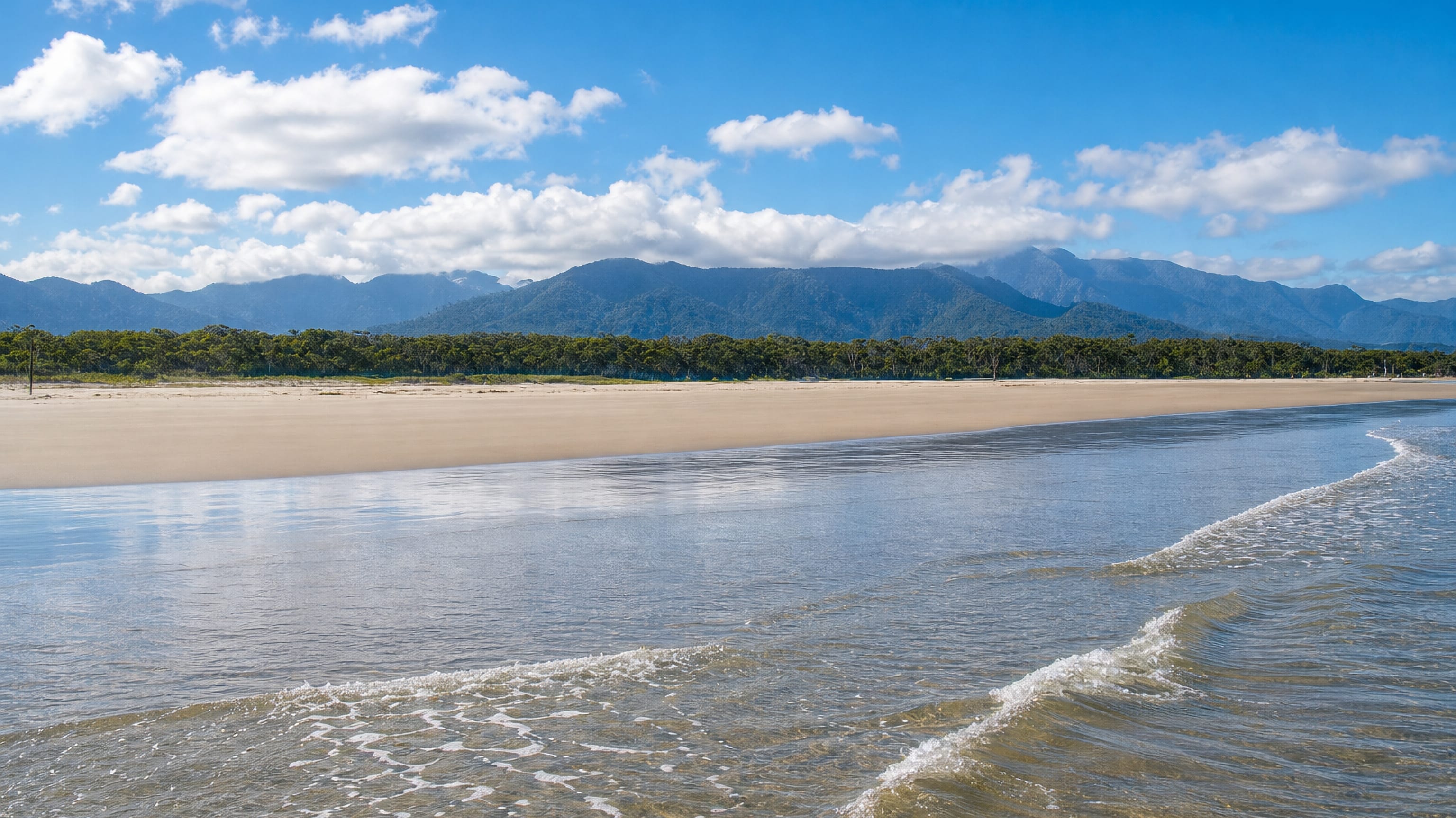 Wide empty sand beach at Bertioga, Brazil, backed by forest and the Serra do Mar ridgeline