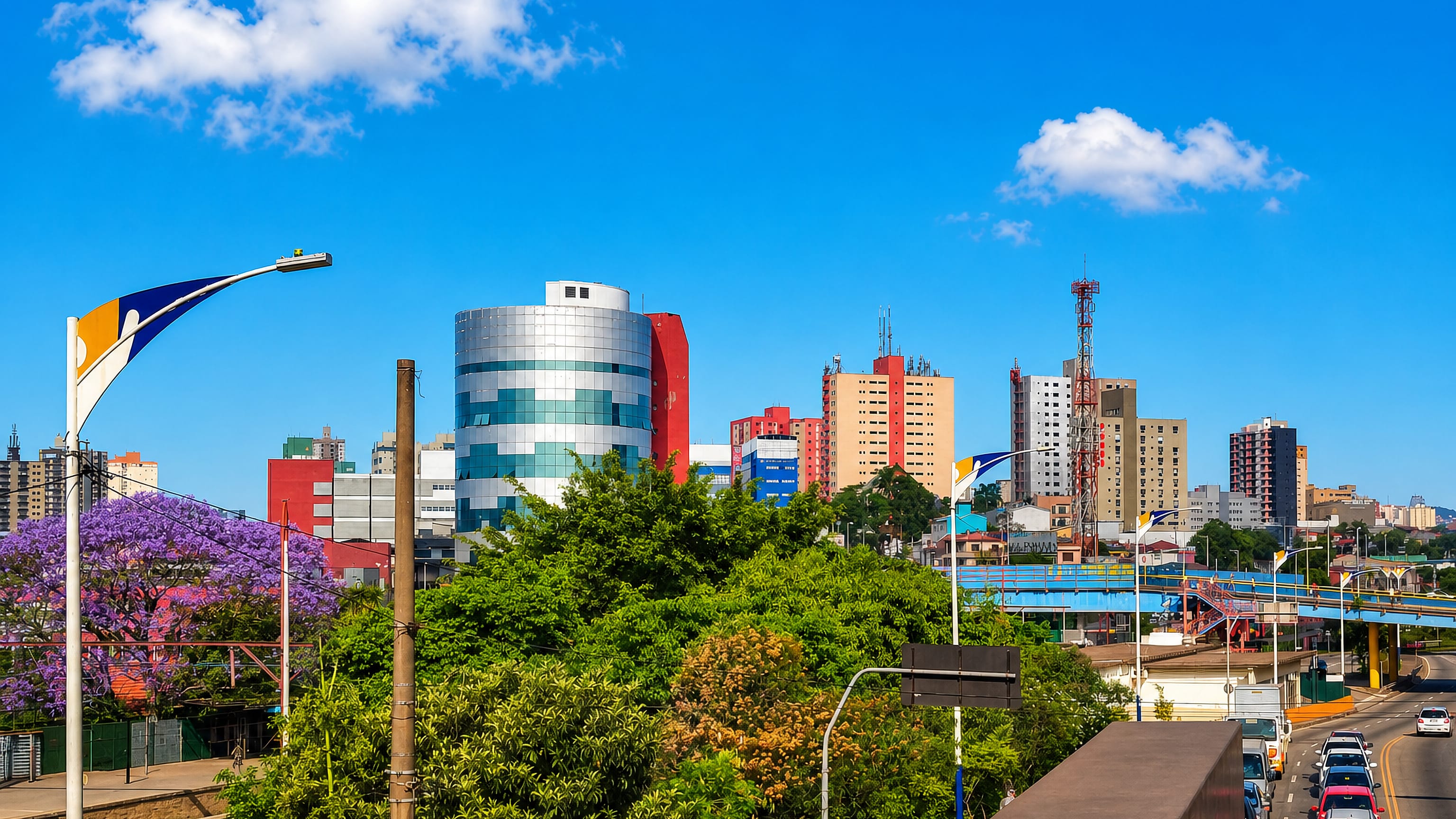 Mid-rise skyline of Mauá, São Paulo, with flowering jacaranda trees and a busy avenue below.