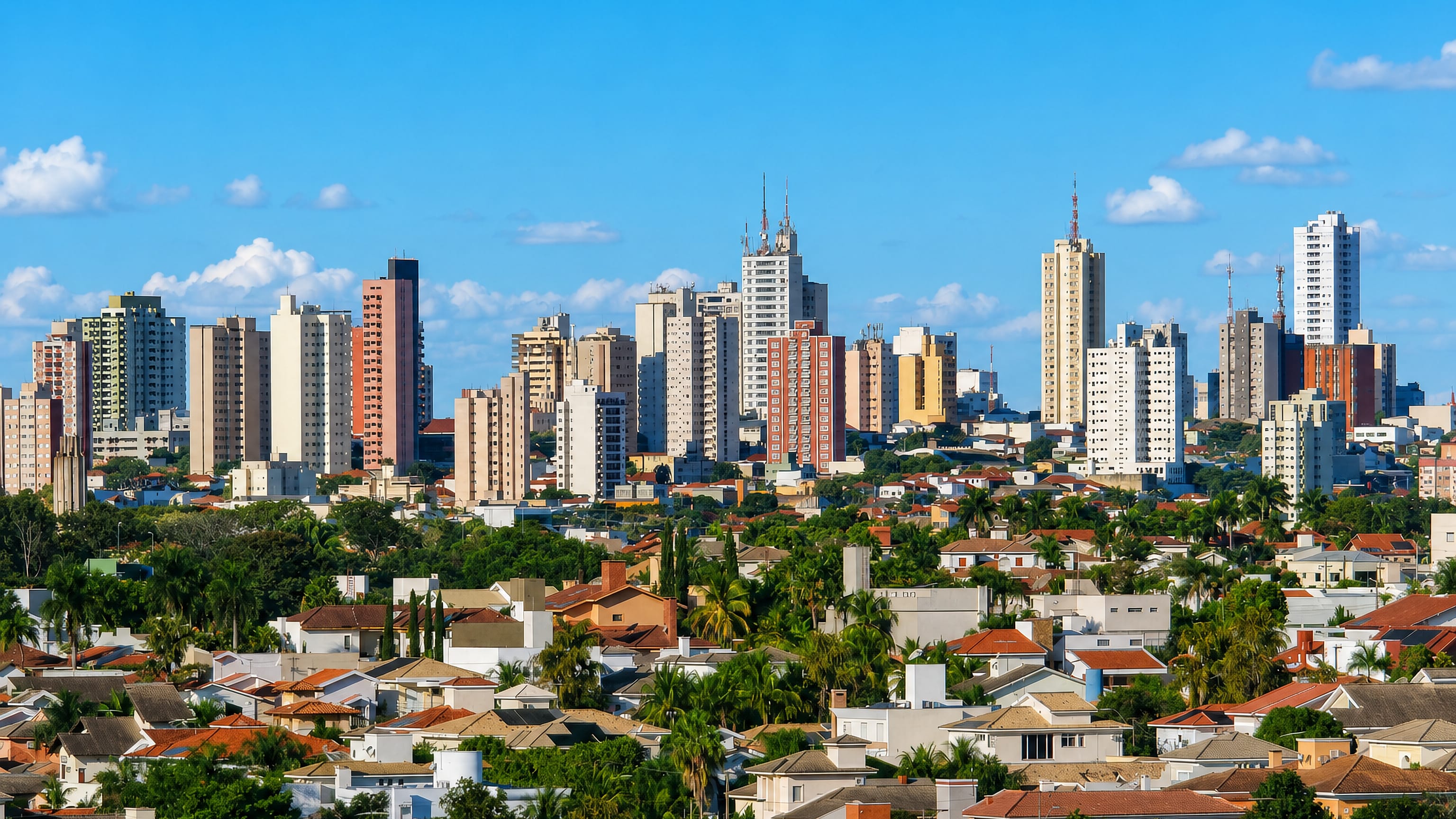 Skyline of Presidente Prudente, Brazil, with residential towers rising above tile-roofed houses and palms