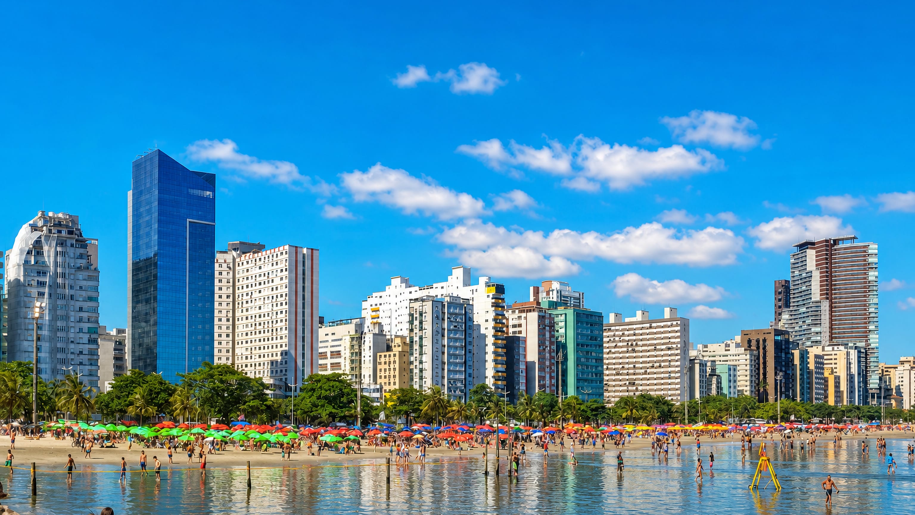 Santos beachfront in Brazil with high-rise towers, palm-lined shore and colourful umbrellas by the sea.