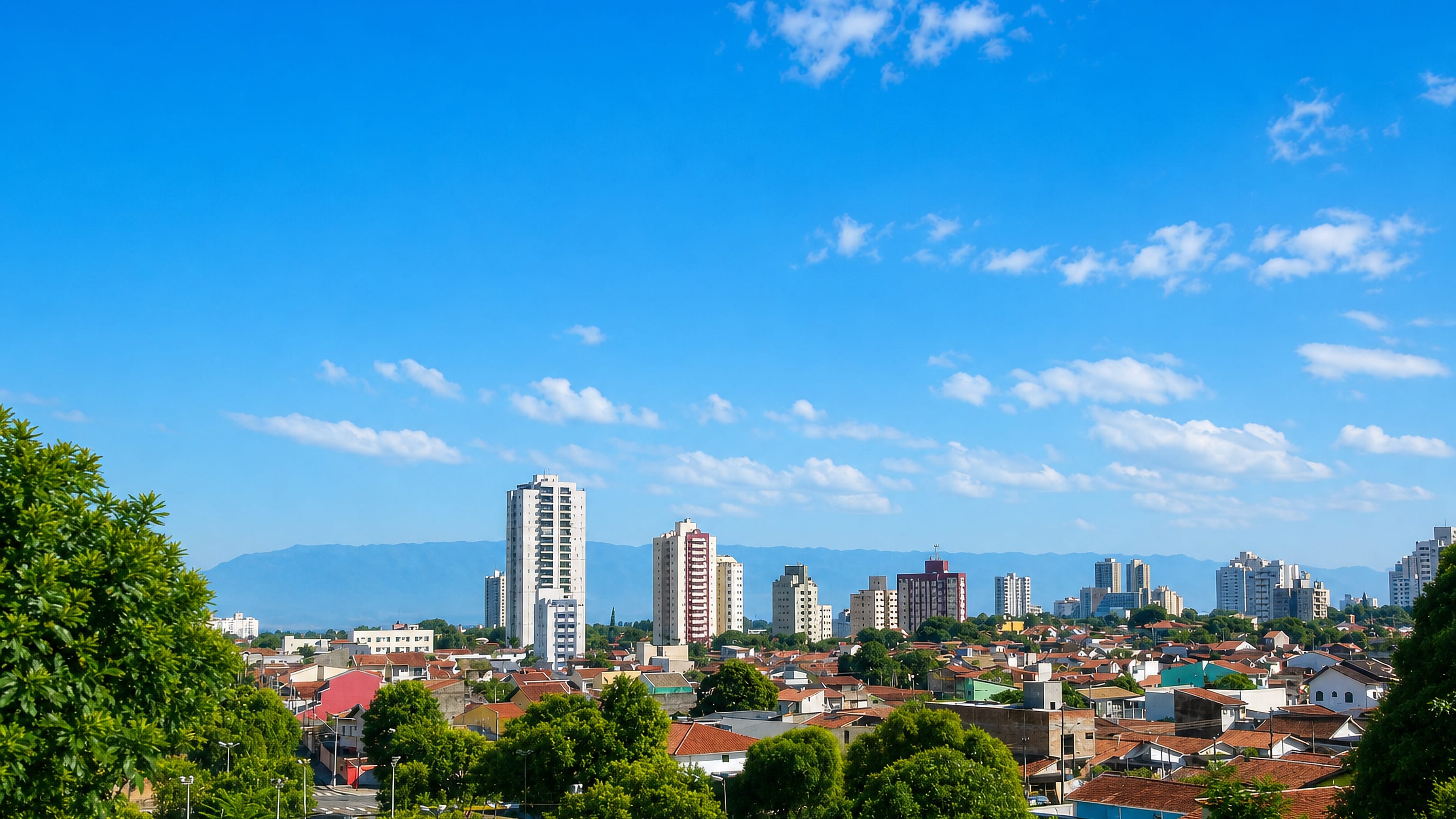 Taubate skyline in Brazil's Paraiba Valley, apartment towers above red-tiled roofs with mountains behind.