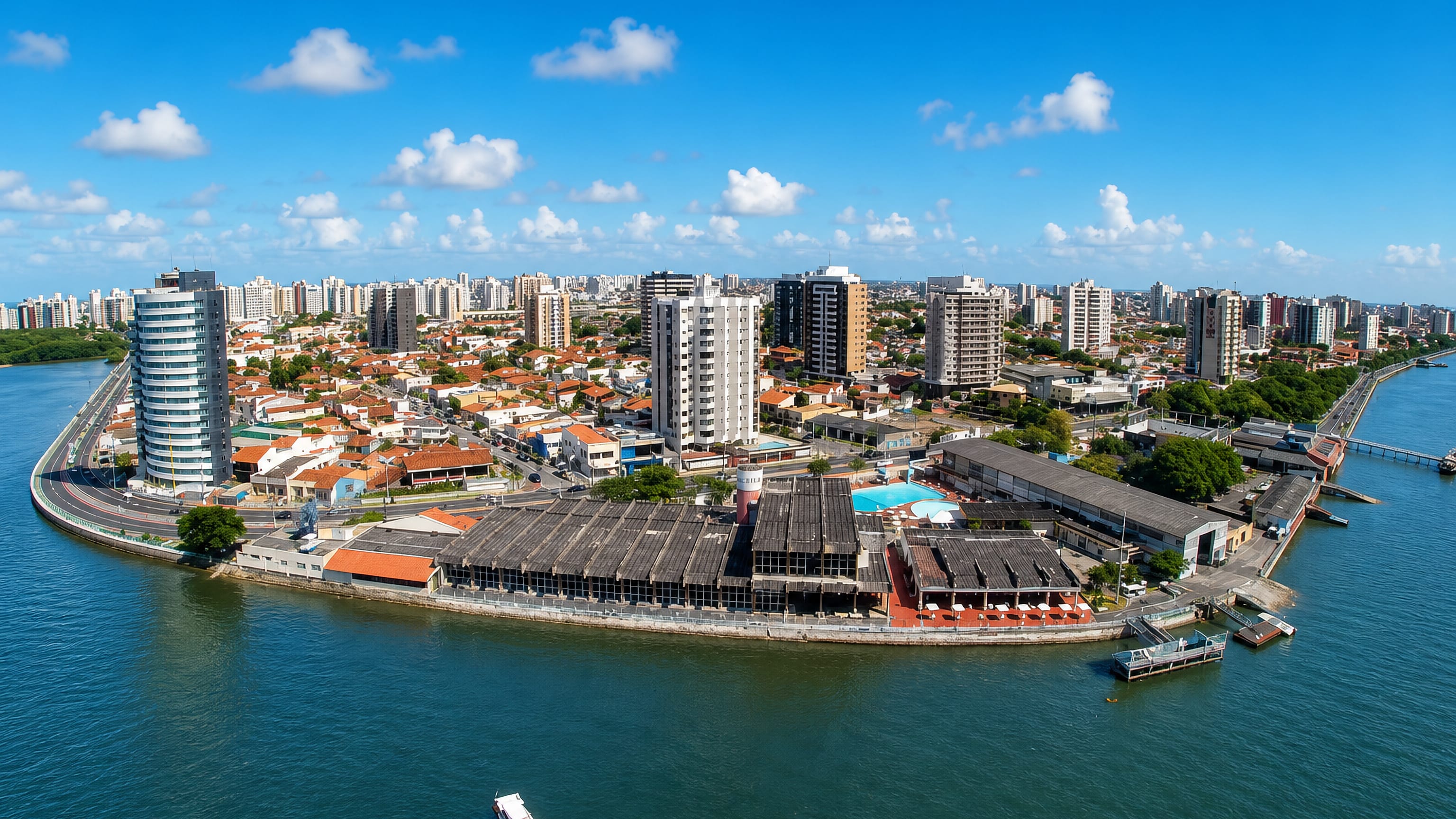 Aerial view of Aracaju's riverfront point on the Sergipe, with apartment towers, warehouse sheds and a boat.
