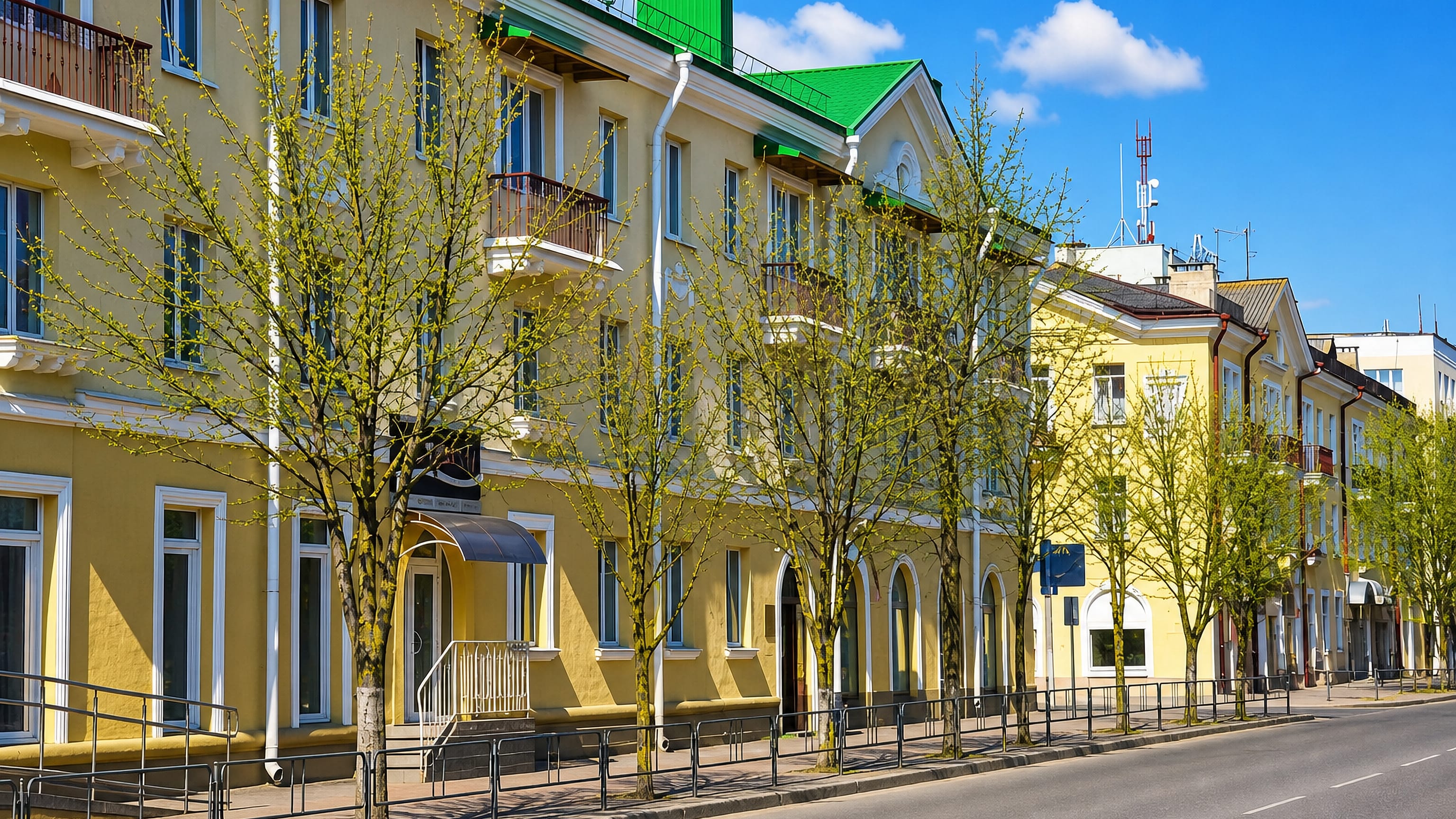 Sunlit yellow post-war apartment blocks lining a quiet tree-lined avenue in central Baranovichi, Belarus.