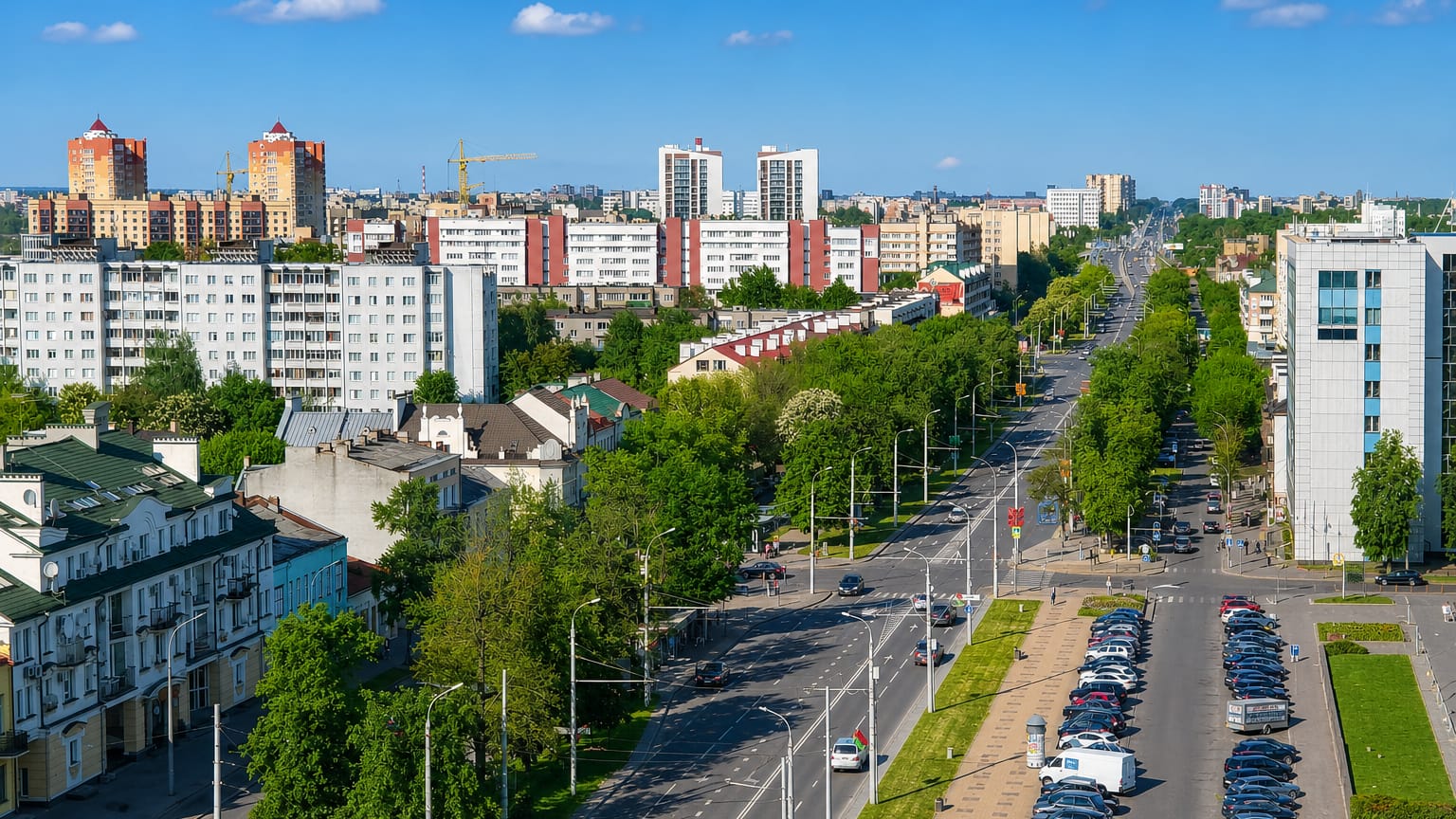 Brest, Belarus, a tree-lined avenue flanked by Soviet-era apartment blocks and parked cars under blue sky.