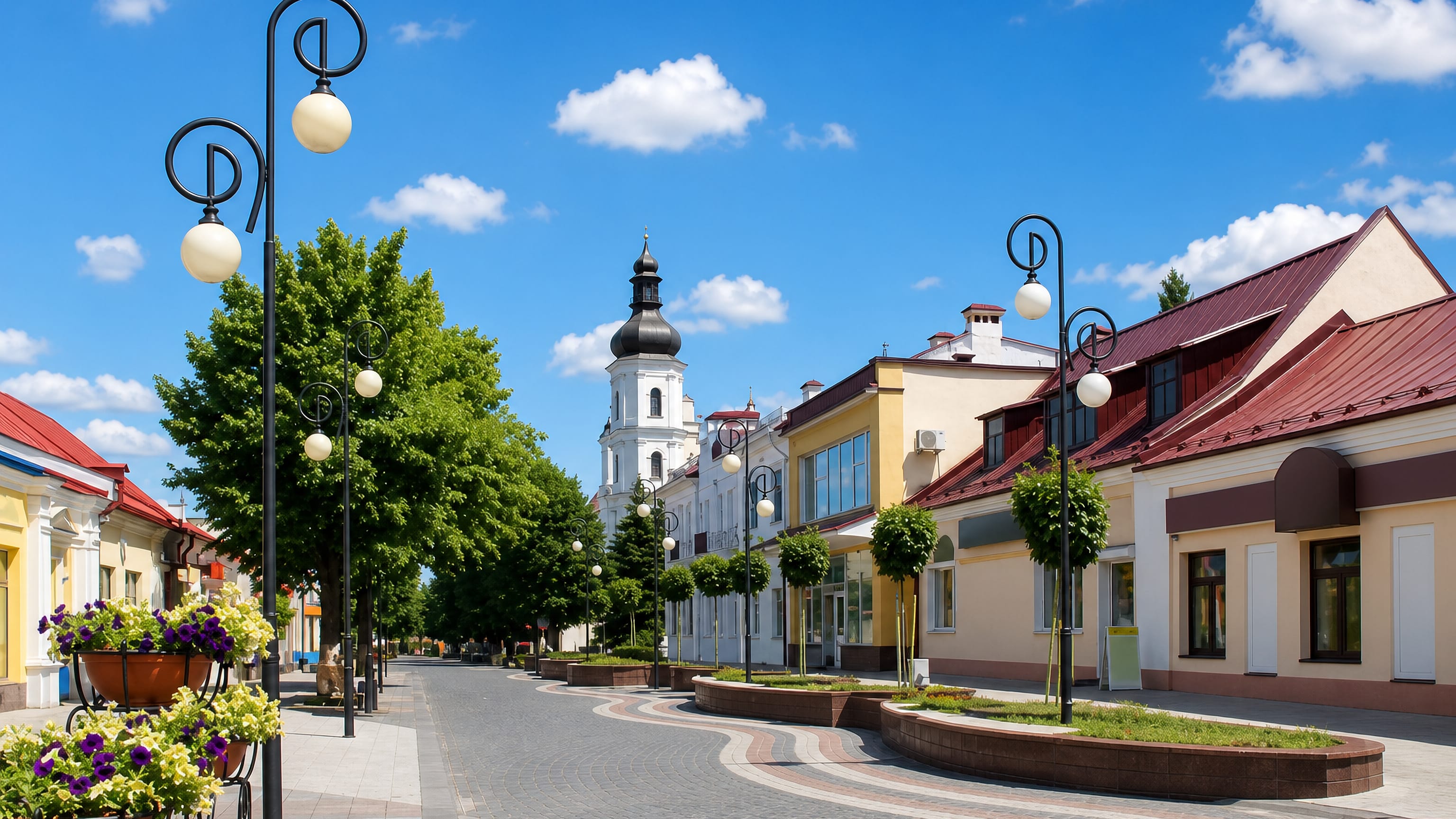 Pinsk pedestrian street lined with pastel townhouses, leading to the white cathedral belfry with its dark dome.