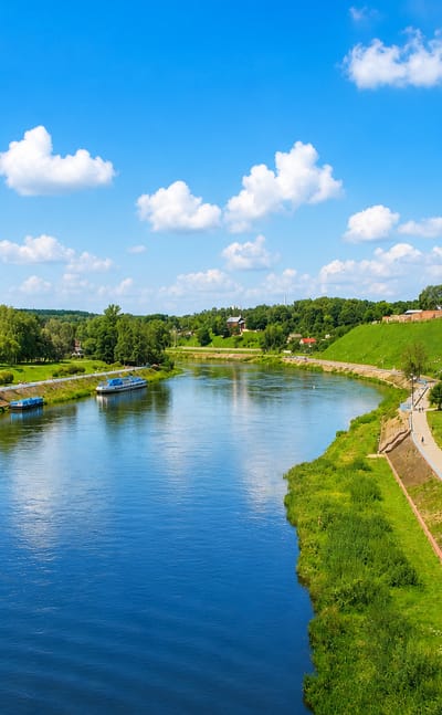 Tour boats on the Neman River below Hrodna's hilltop castle and palace complex under a summer sky.