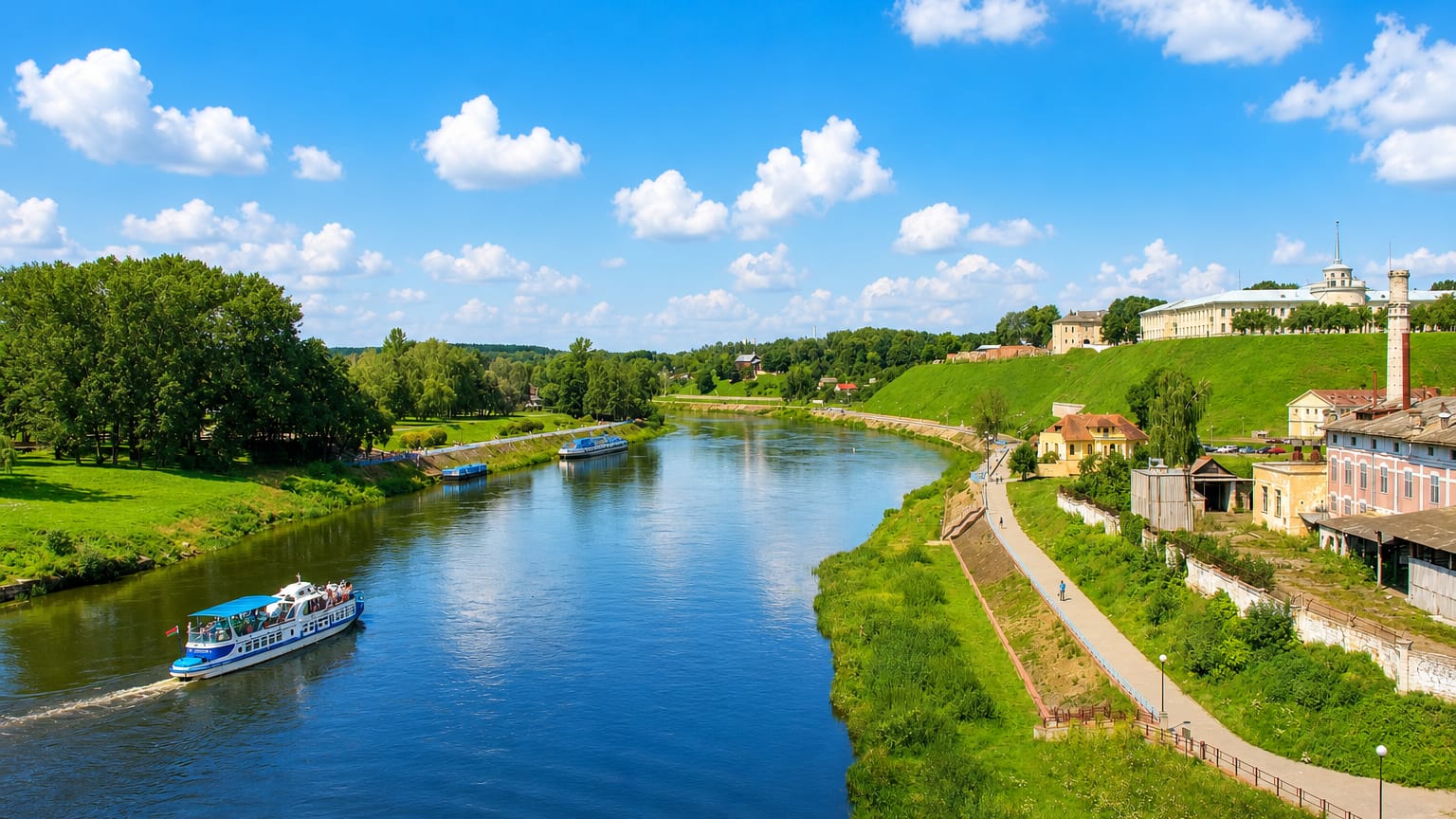 Tour boats on the Neman River below Hrodna's hilltop castle and palace complex under a summer sky.