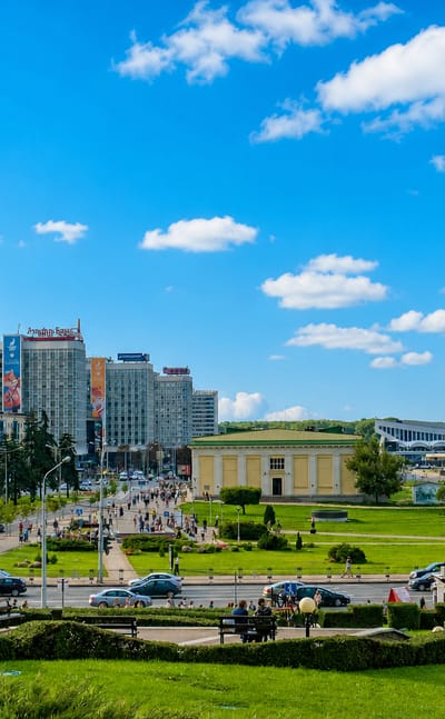 Minsk cityscape with the glass BSB tower rising above Pobediteley Avenue and landscaped park greenery.