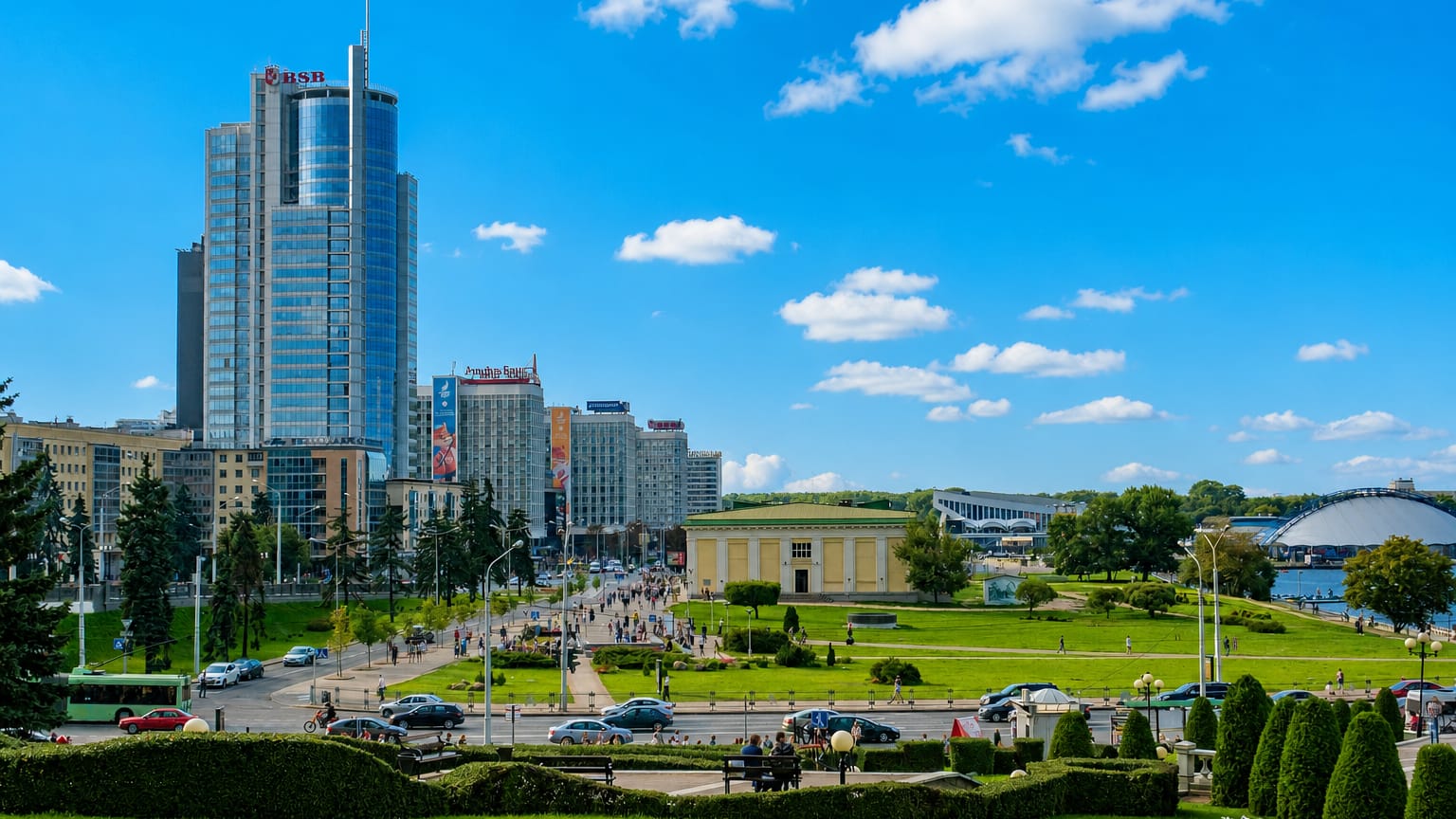 Minsk cityscape with the glass BSB tower rising above Pobediteley Avenue and landscaped park greenery.