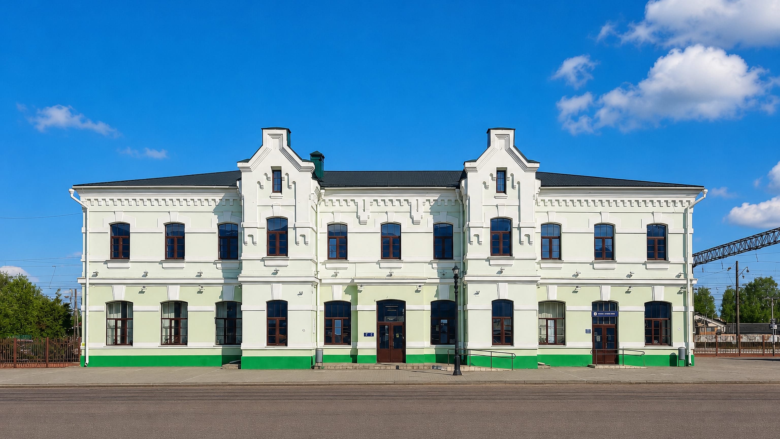 Green-and-white historic railway station building in Barysaw, Belarus, seen across an empty road.