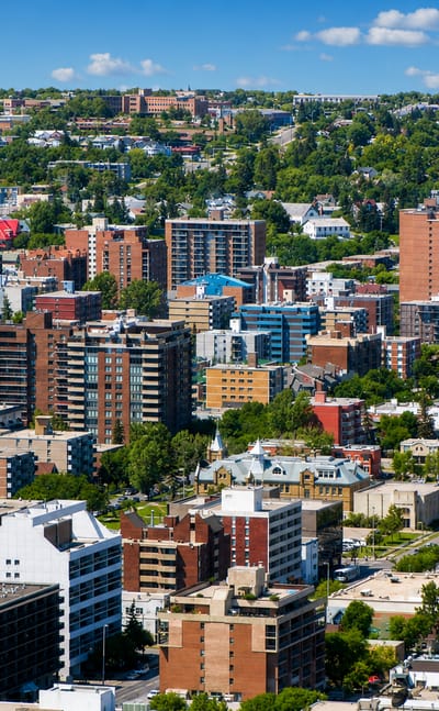 Dense inner-city Calgary district of mid-rise apartments and offices with tree-lined streets and hills on the horizon.