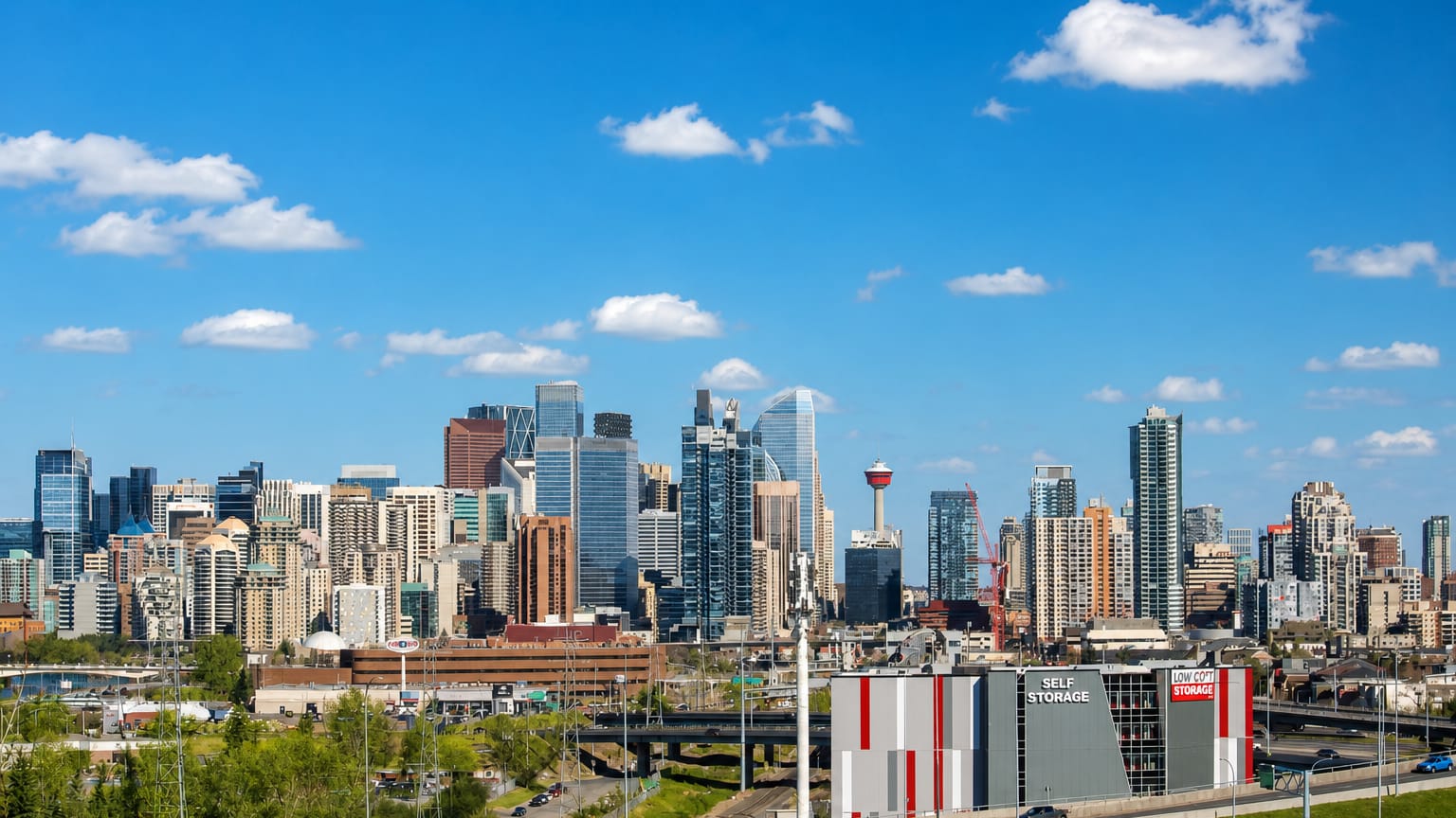 Calgary's downtown skyline and Calgary Tower rising beyond a highway and storage building near Bowness.