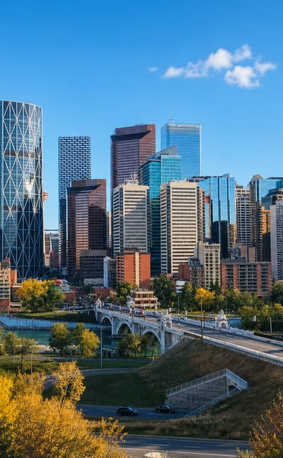 Downtown Calgary skyline with the curved Bow tower and Centre Street Bridge seen from the Crescent Heights bluff amid autumn trees.