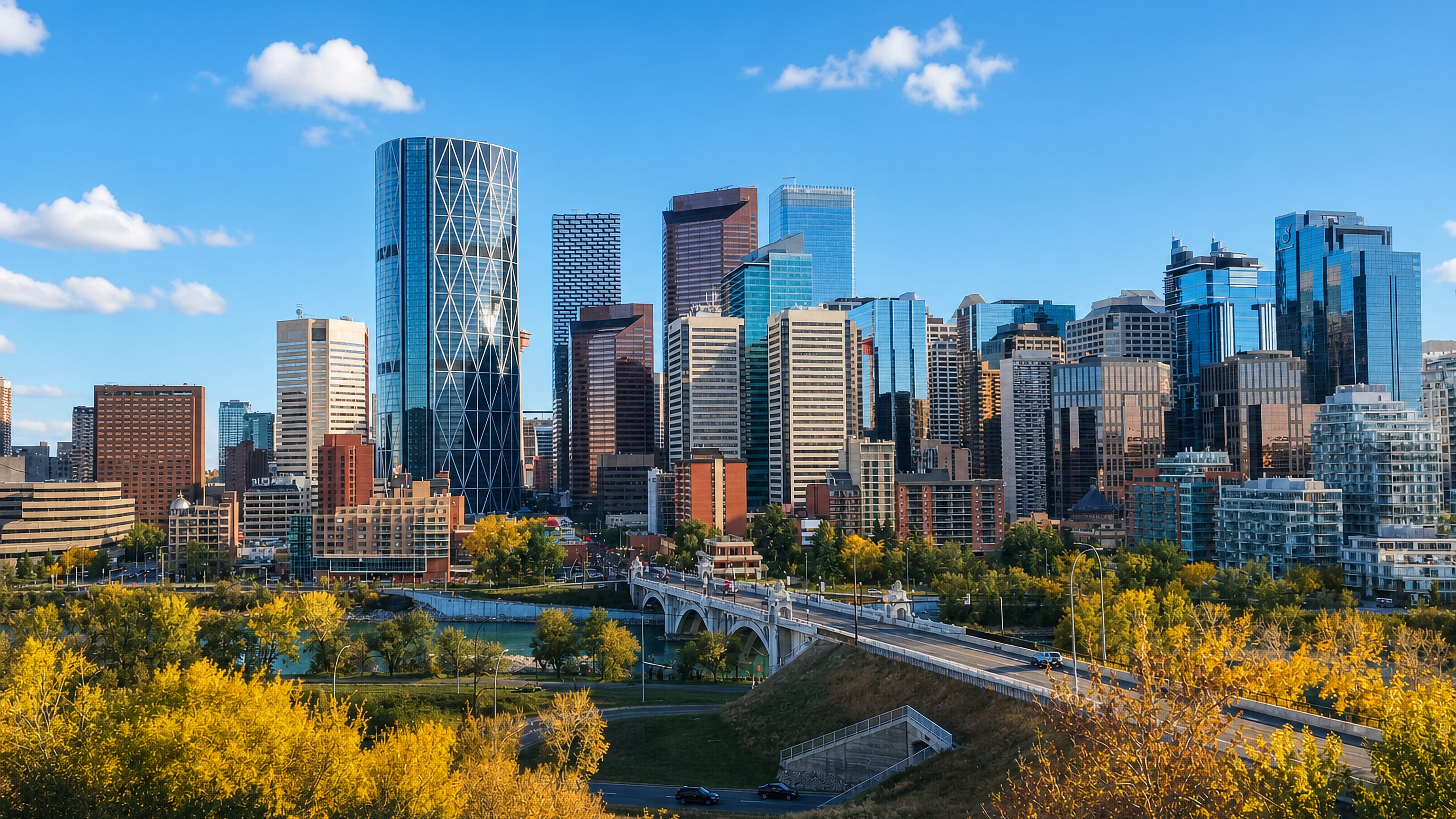 Downtown Calgary skyline with the curved Bow tower and Centre Street Bridge seen from the Crescent Heights bluff amid autumn trees.