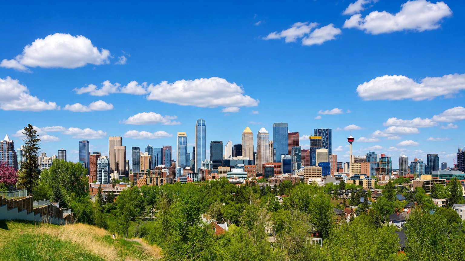Downtown Calgary skyline with the Calgary Tower rising above office towers, framed by green trees under a bright blue sky.