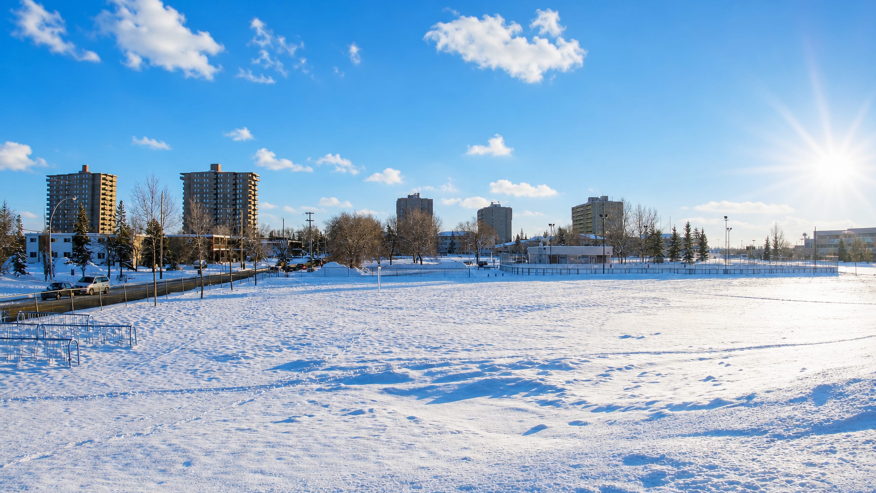 Snow-covered open field backed by apartment towers in Empire Park, Edmonton, on a bright winter day.