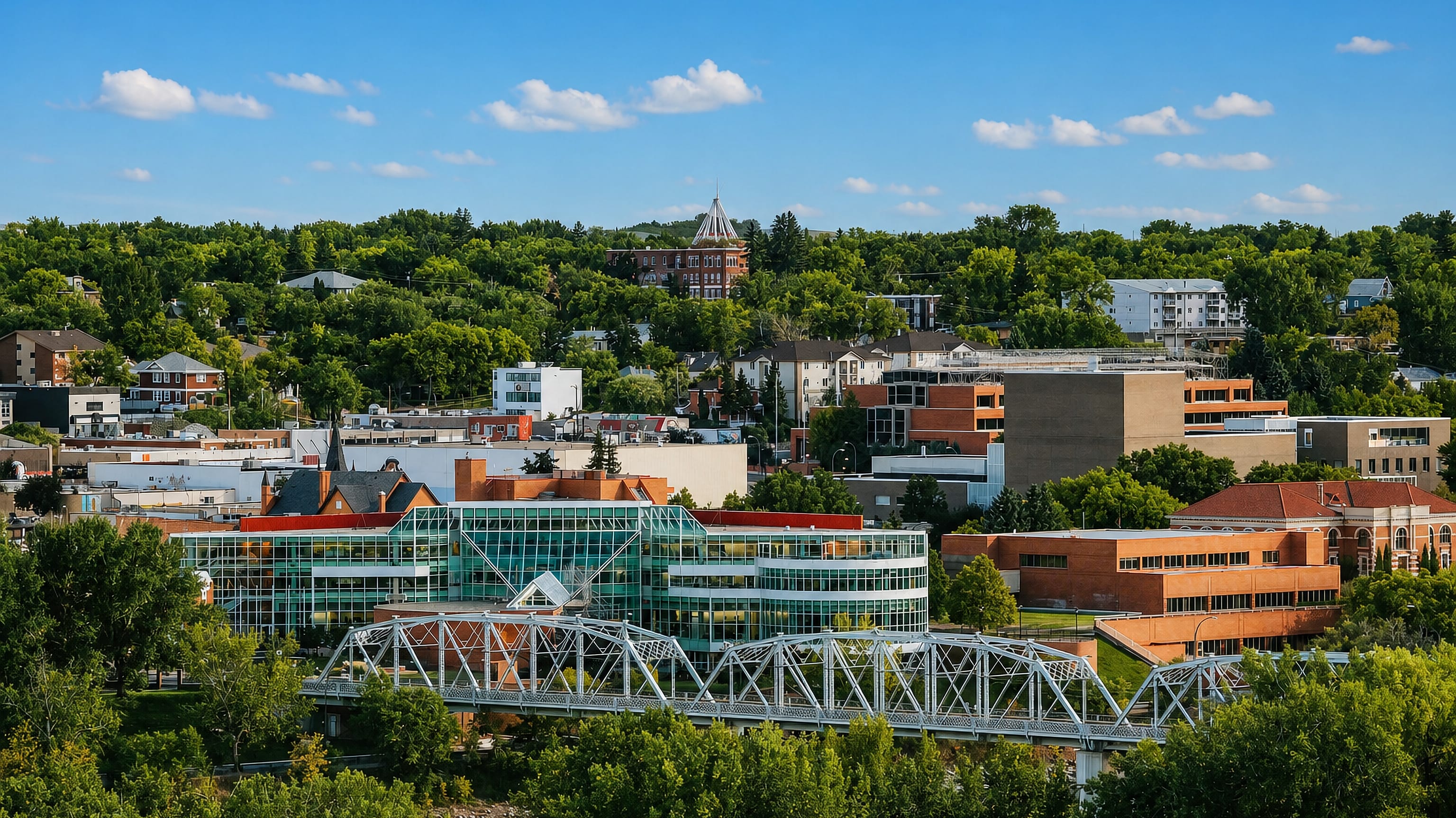 Medicine Hat, Alberta, a steel truss bridge over the river below the leafy downtown and its glass civic building.