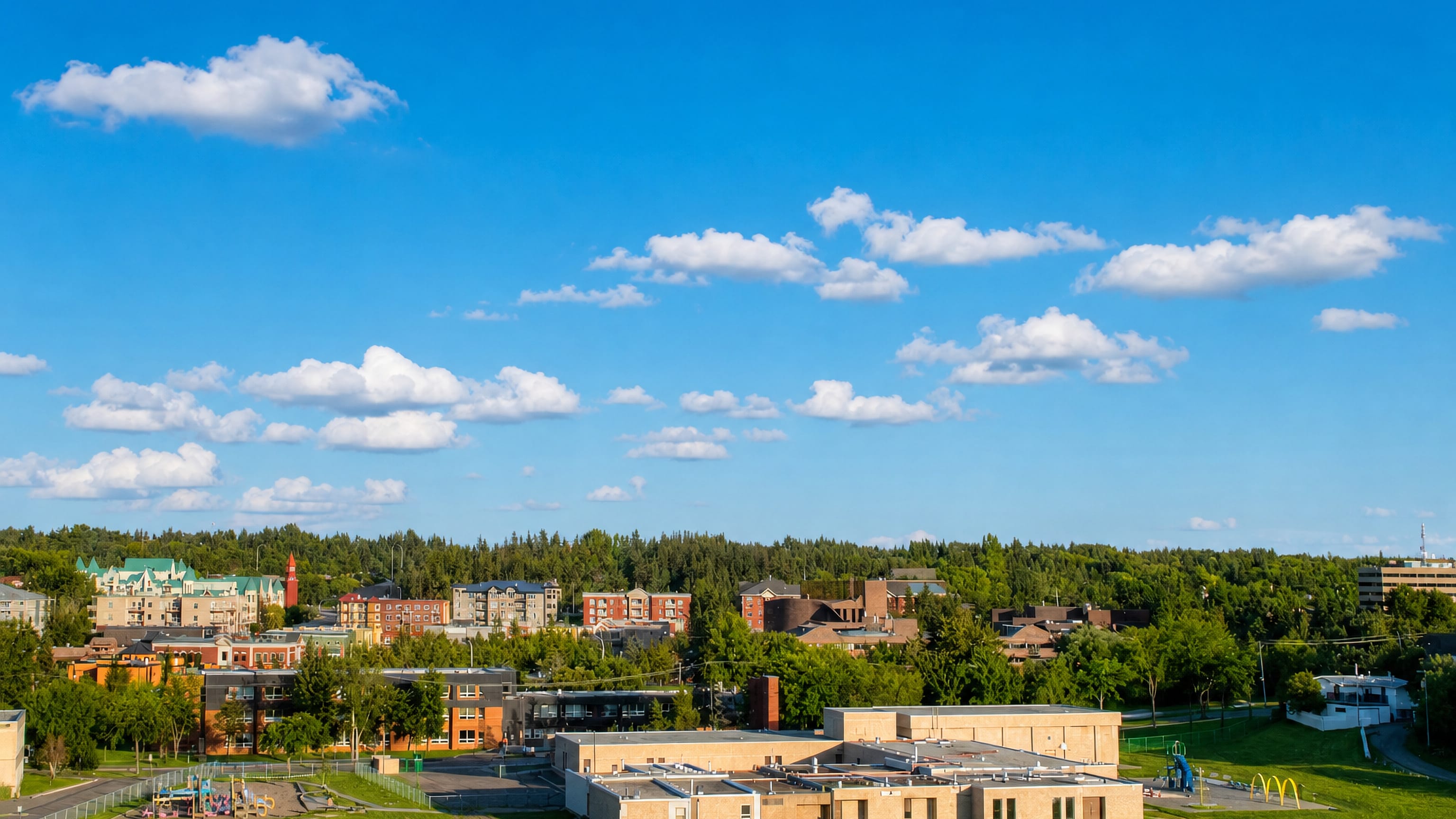 Low-rise streets, green roofs and a brick tower among trees across St. Albert, Alberta.