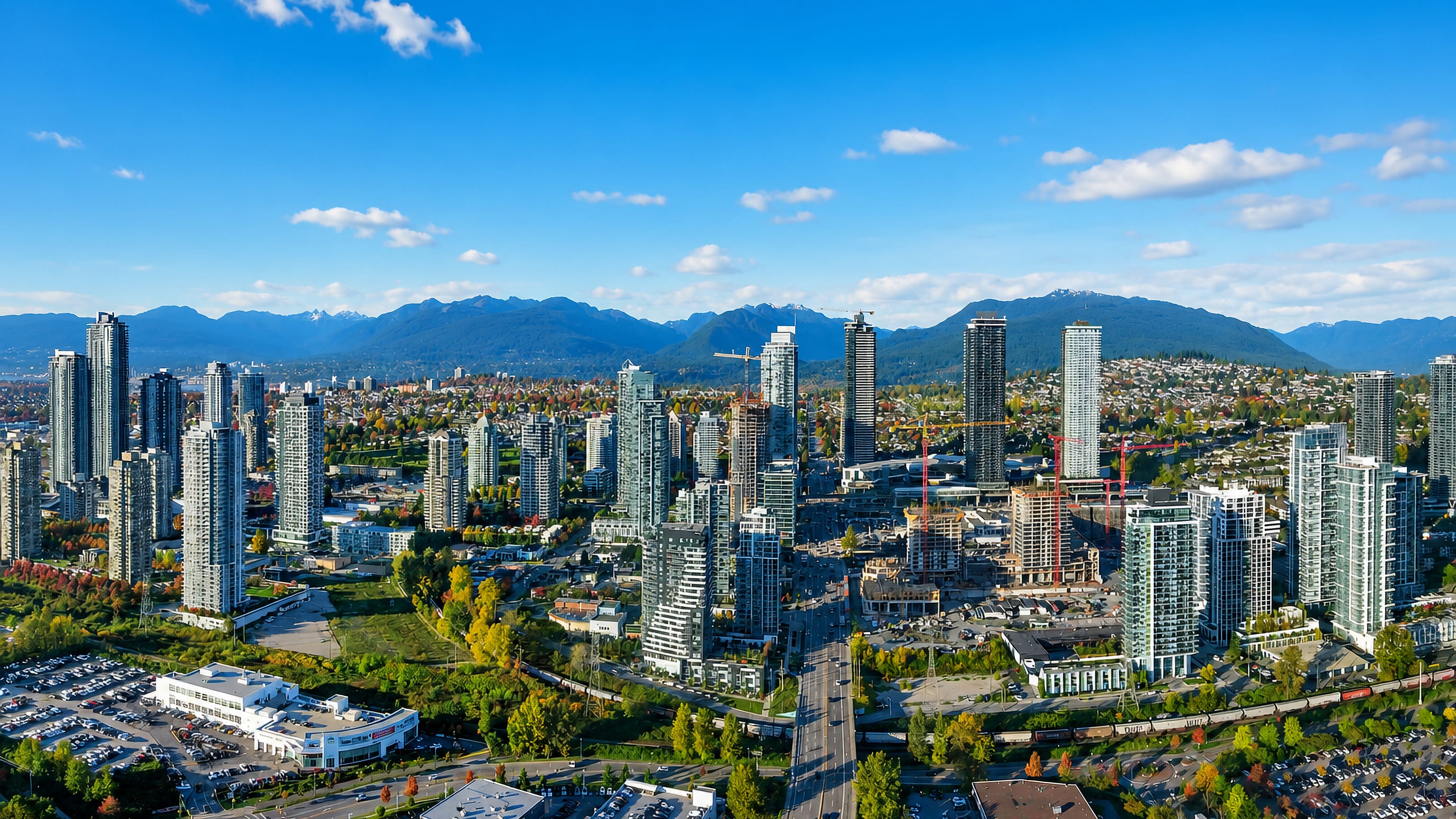 Aerial view of Burnaby's highrise towers and rail corridor with the North Shore Mountains beyond.