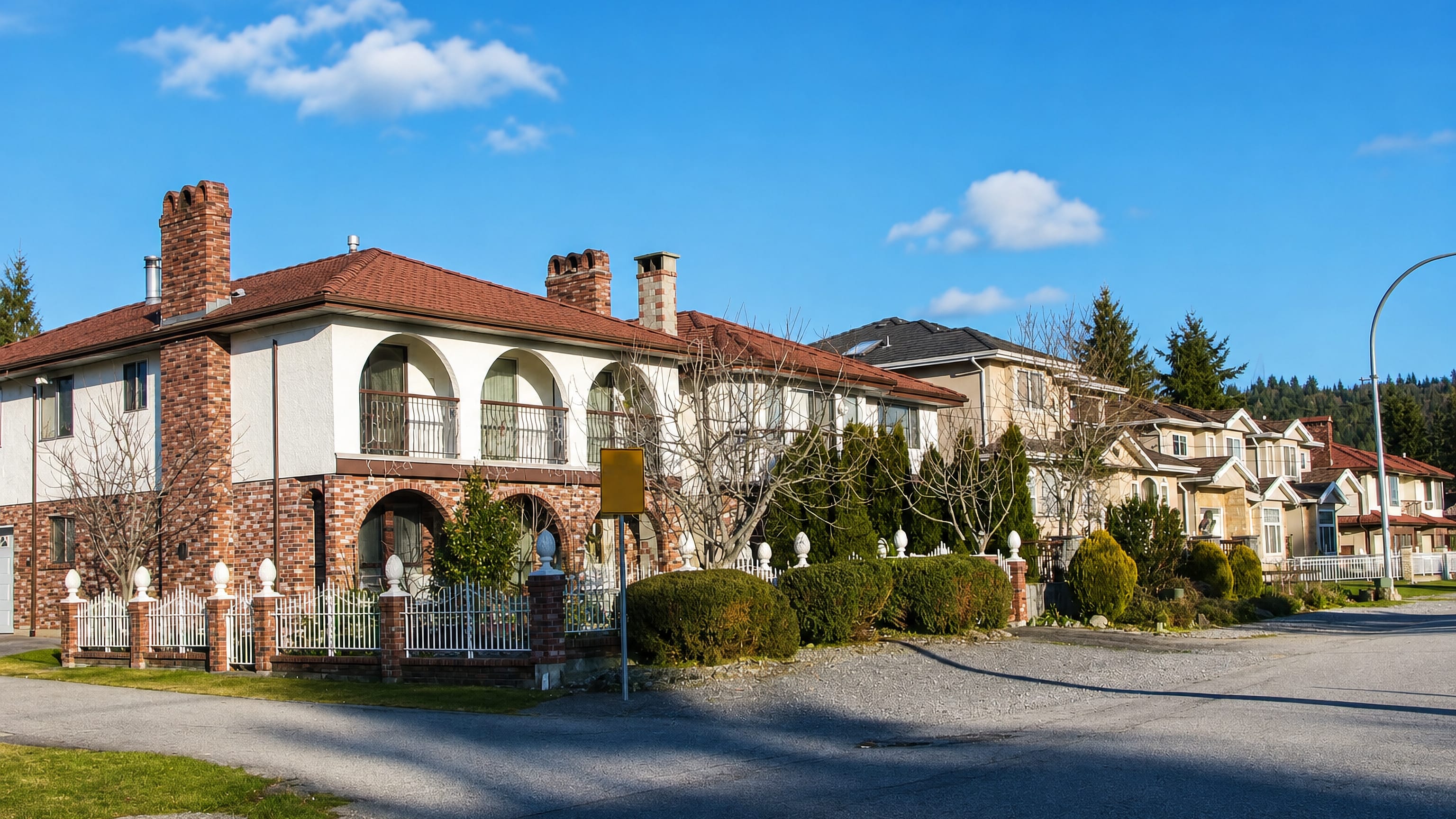 Brick-and-stucco houses with arched balconies along a quiet Lochdale street in Burnaby, British Columbia.