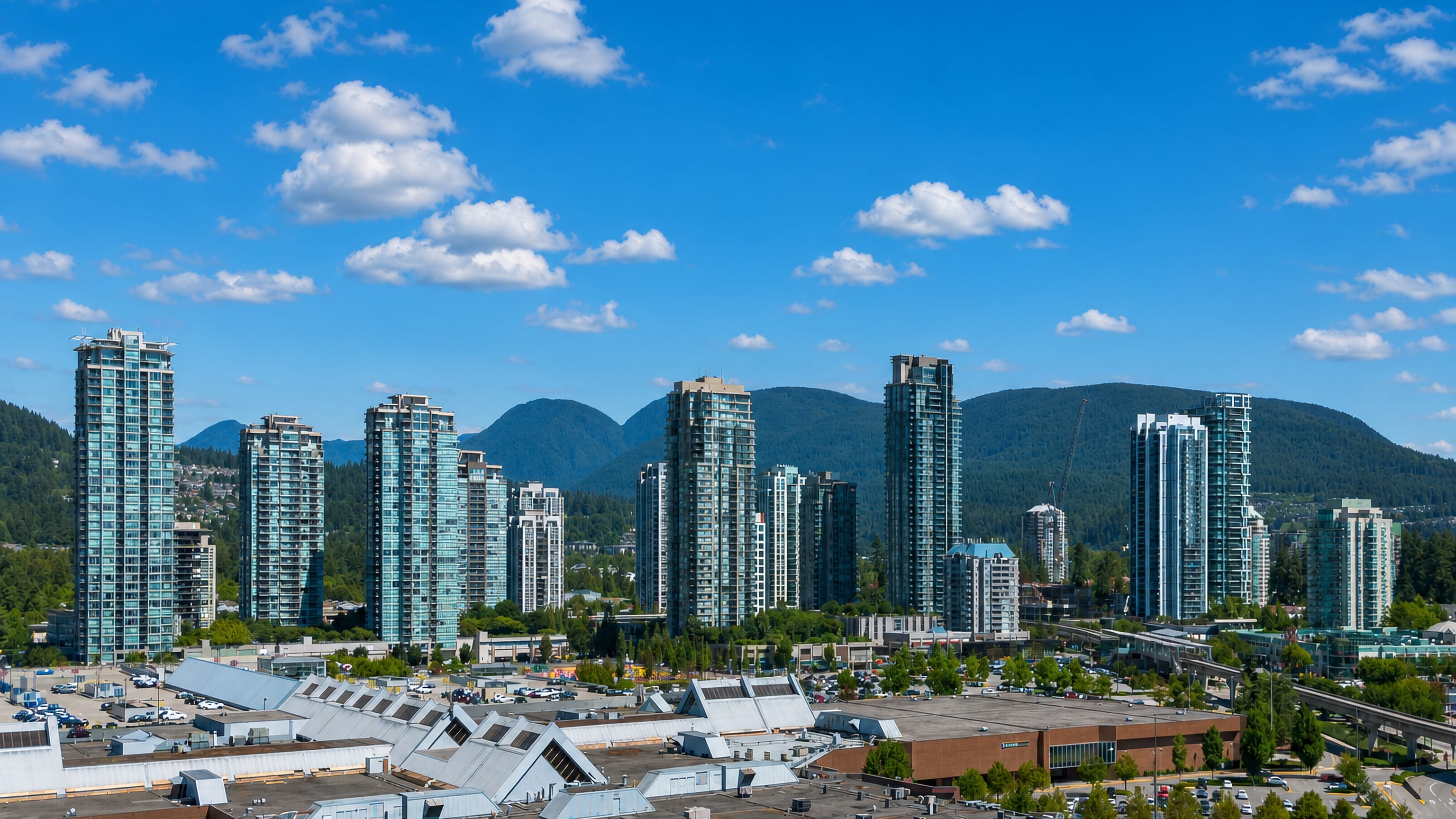 Glass residential towers and a SkyTrain guideway below the Coast Mountains in Coquitlam, British Columbia.
