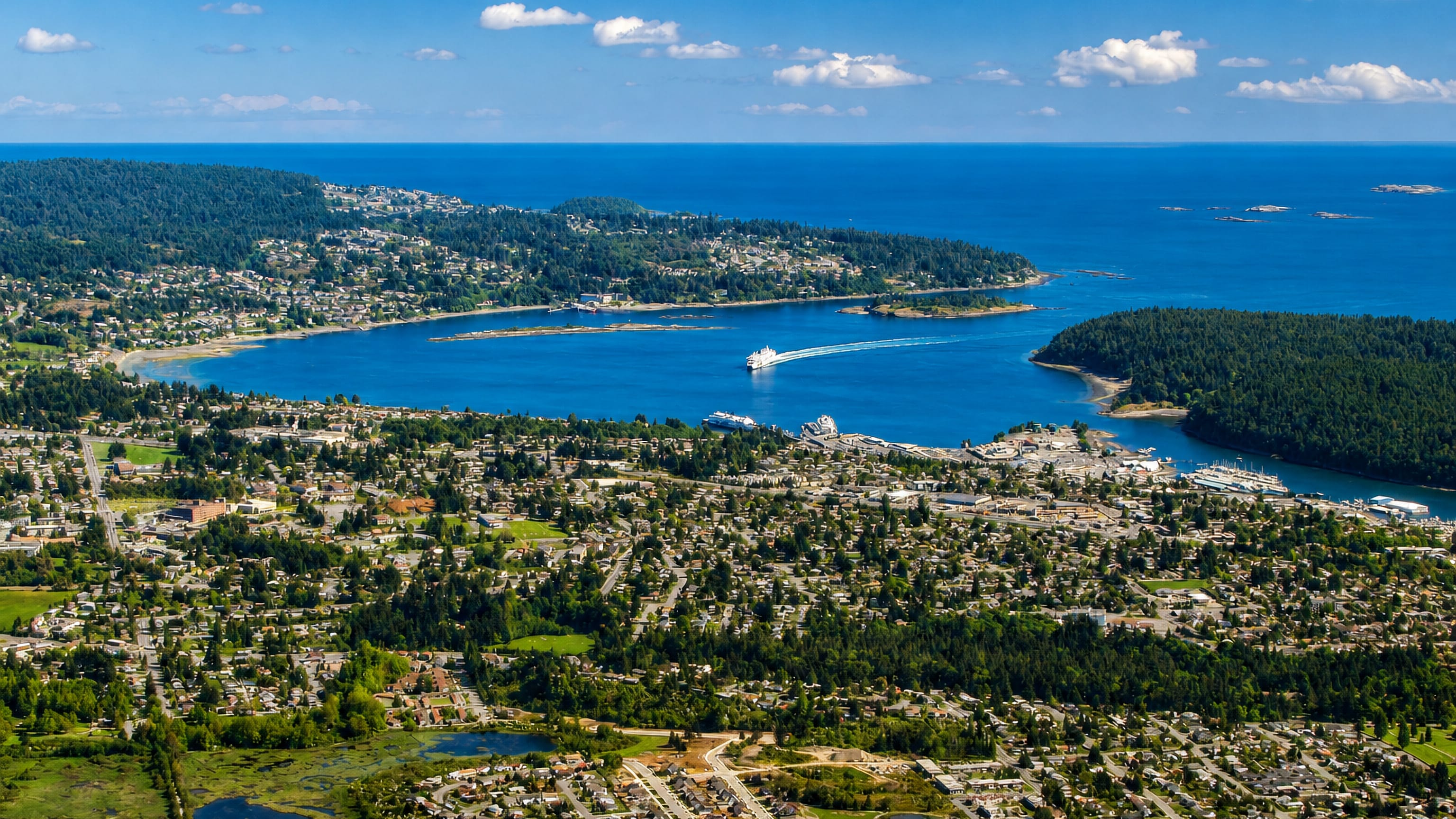 Aerial view over Departure Bay in Nanaimo with a ferry leaving the harbour past forested headlands.