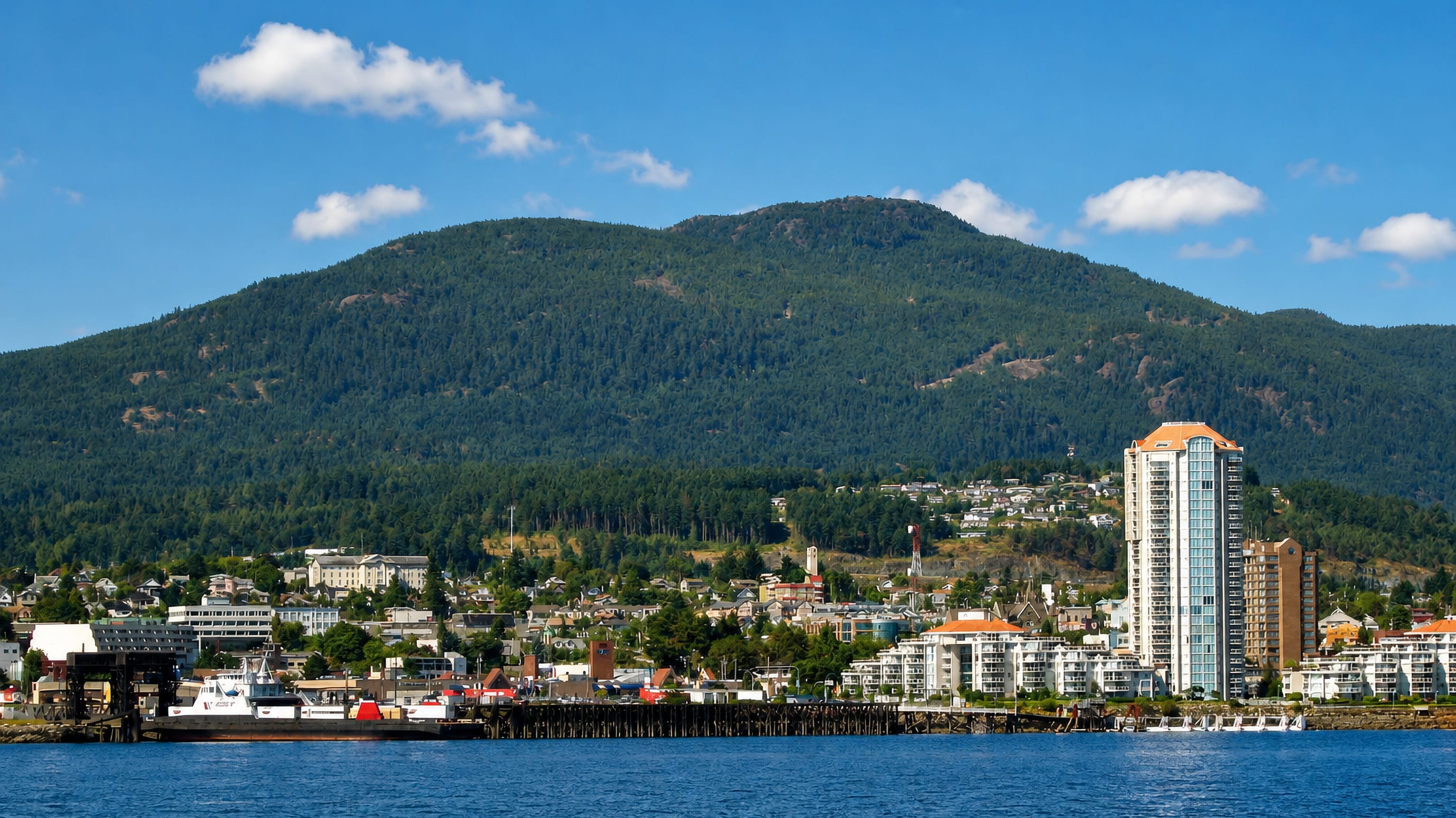 Nanaimo, British Columbia, from the harbour with a waterfront high-rise, ferry dock and forested mountain.