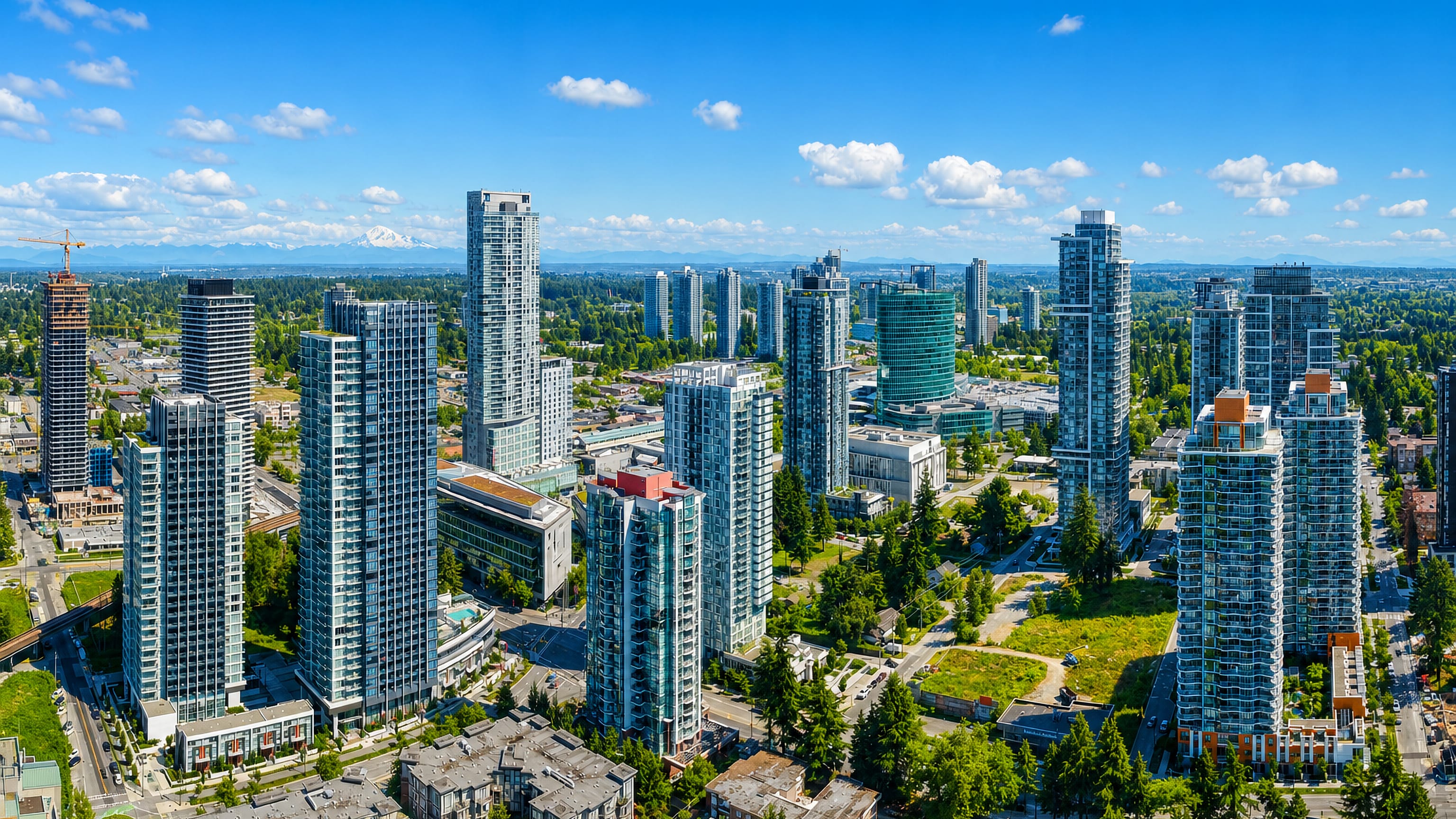 Aerial view of Surrey City Centre's glass condo towers and SkyTrain line with Mount Baker on the horizon