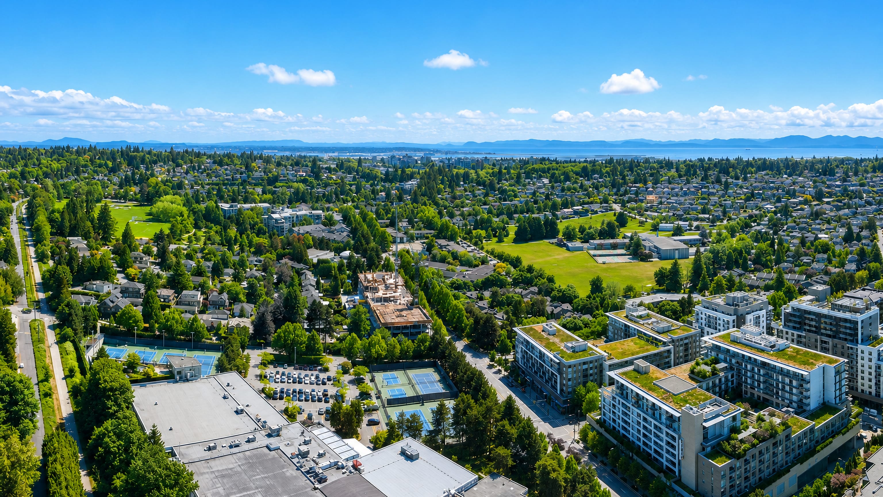Aerial view over Arbutus Ridge in Vancouver, leafy streets and green-roofed mid-rises toward sea and mountains.