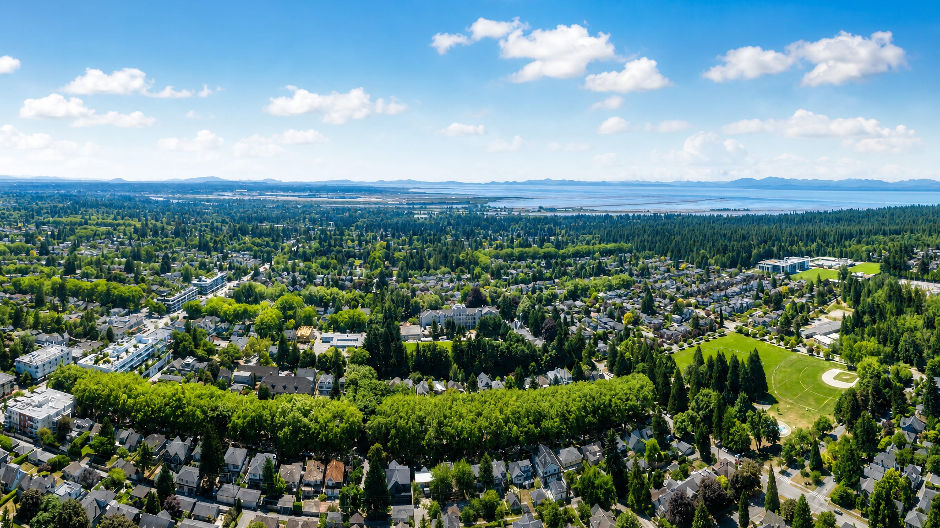 Aerial over the leafy streets and playing fields of Dunbar-Southlands, Vancouver, toward the Strait of Georgia.