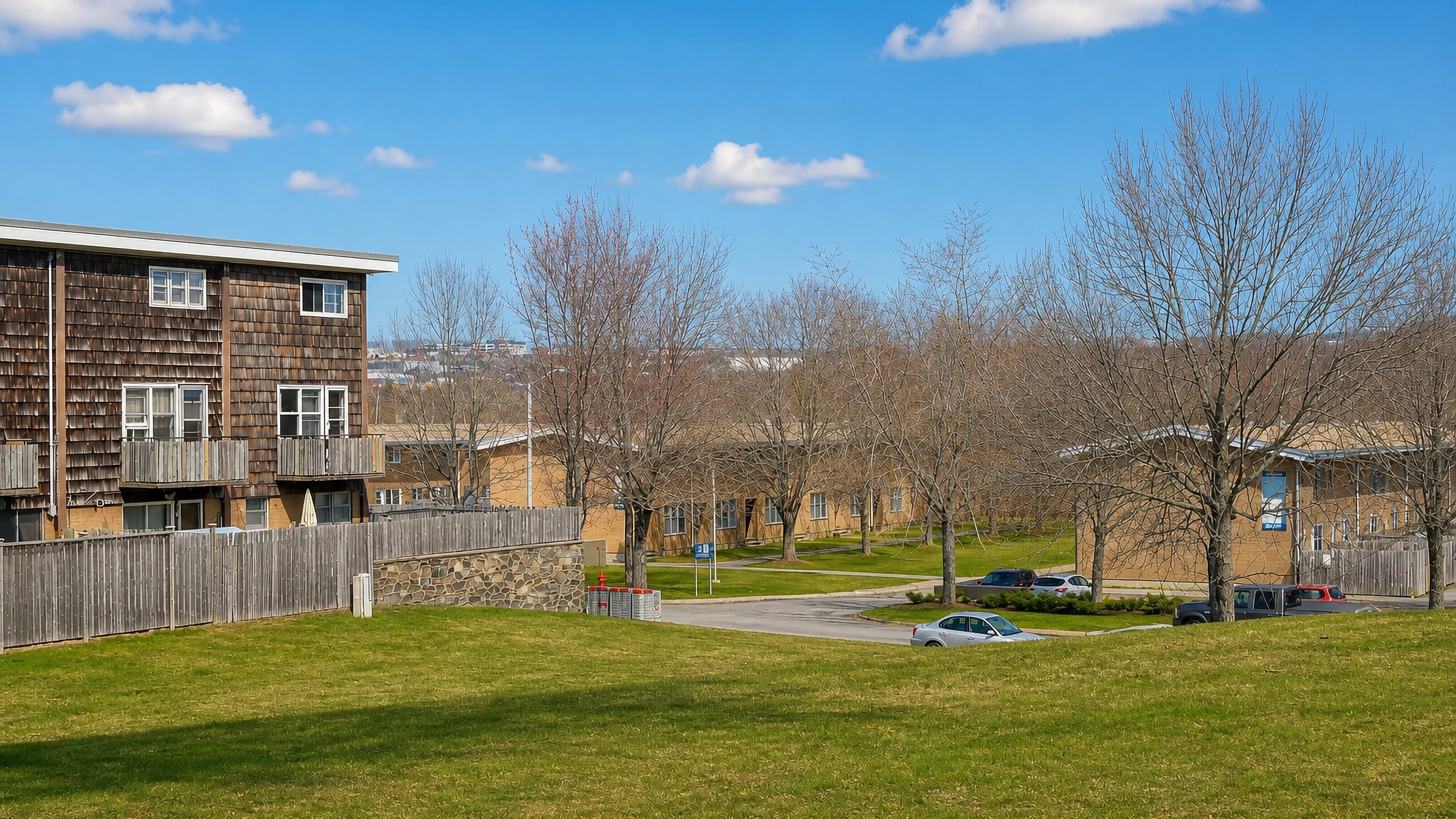 Shingle-clad low-rise apartments and a grassy slope in Wallace Heights, Dartmouth, Nova Scotia, on a clear day.