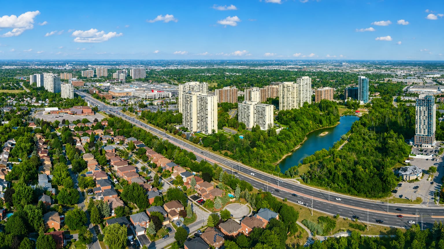 Aerial view of Brampton's apartment tower clusters and tree-lined suburban homes beside a highway and pond.
