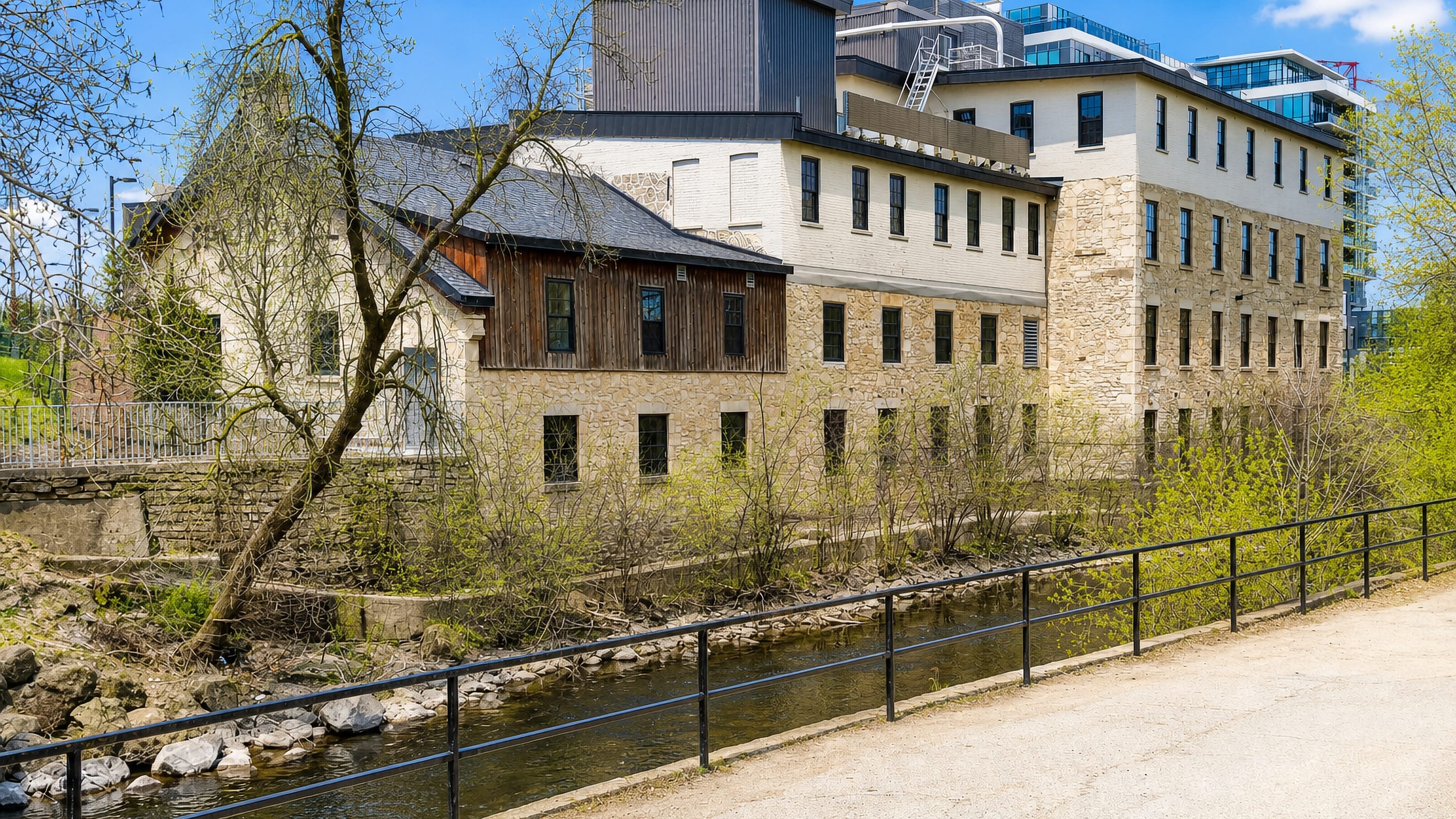 Restored limestone mill buildings above the Speed River in Guelph, Ontario, with a riverside gravel trail.