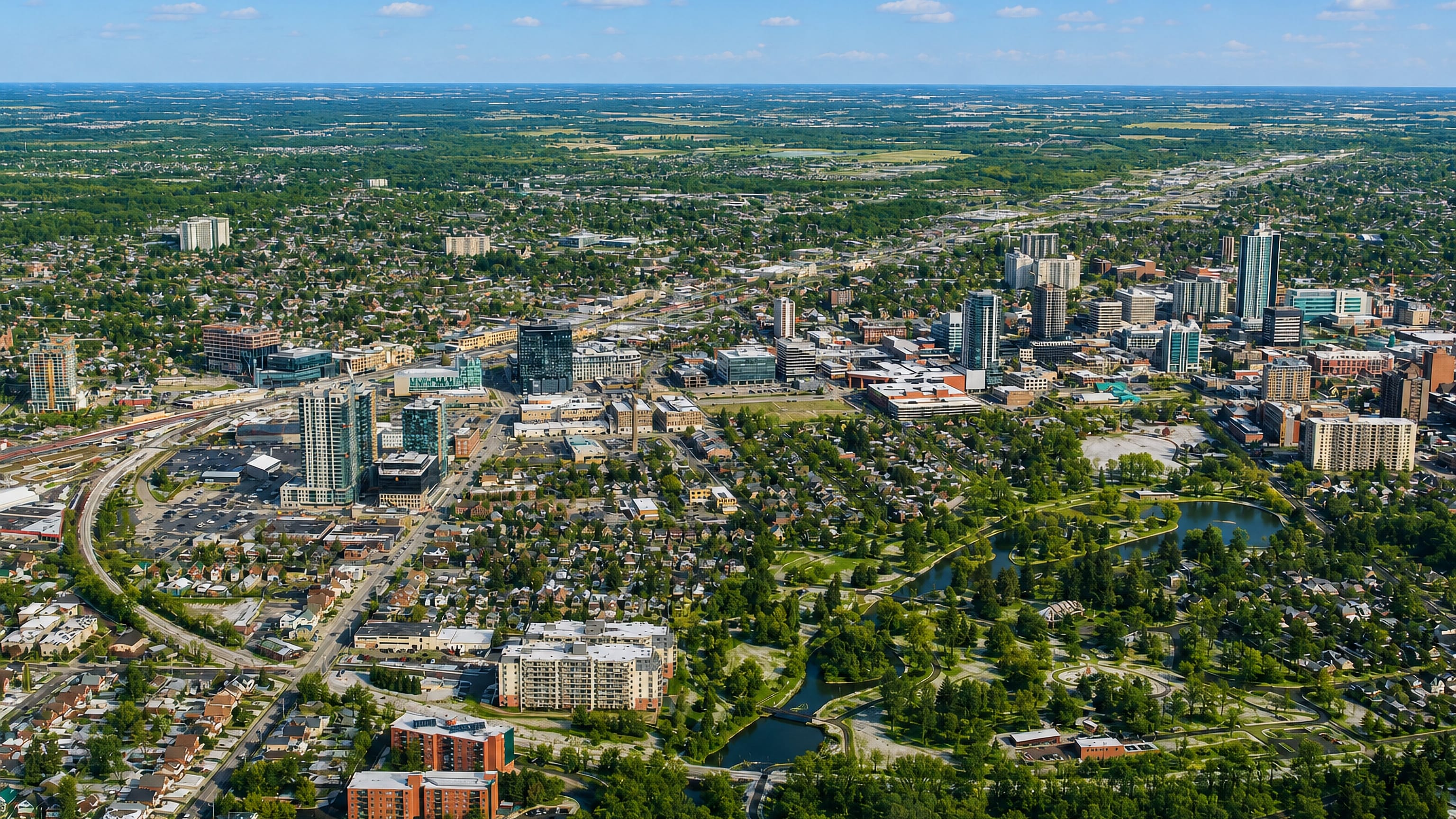 Aerial view of downtown Kitchener, Ontario, with glass towers, leafy neighbourhoods and a lakeside park.