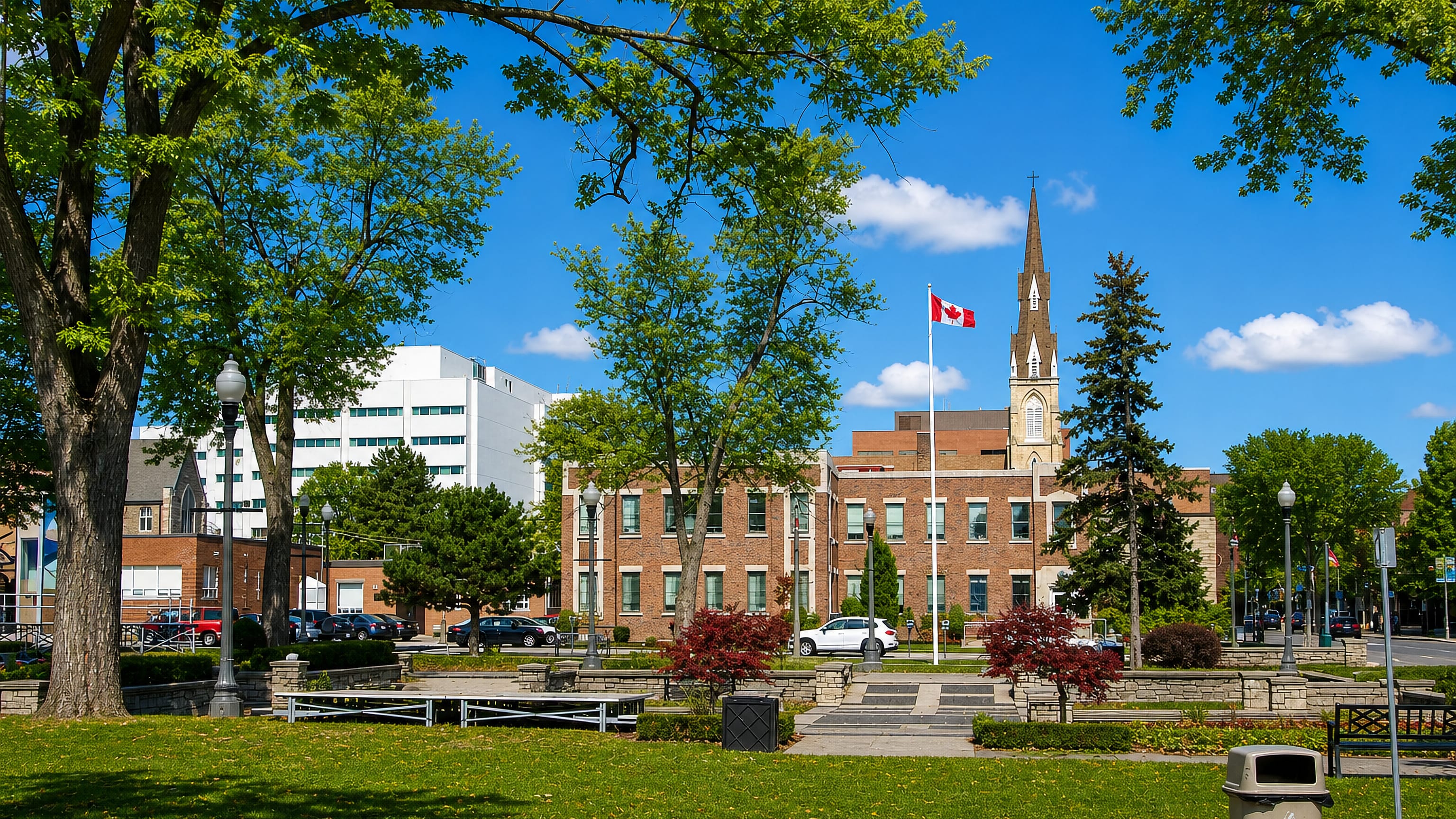 Downtown Oshawa, Ontario, a green park with the Canadian flag, brick civic buildings and a church spire.