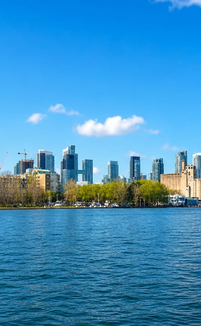 Toronto's downtown skyline with the CN Tower seen across Lake Ontario from a waterfront pier under a blue sky.