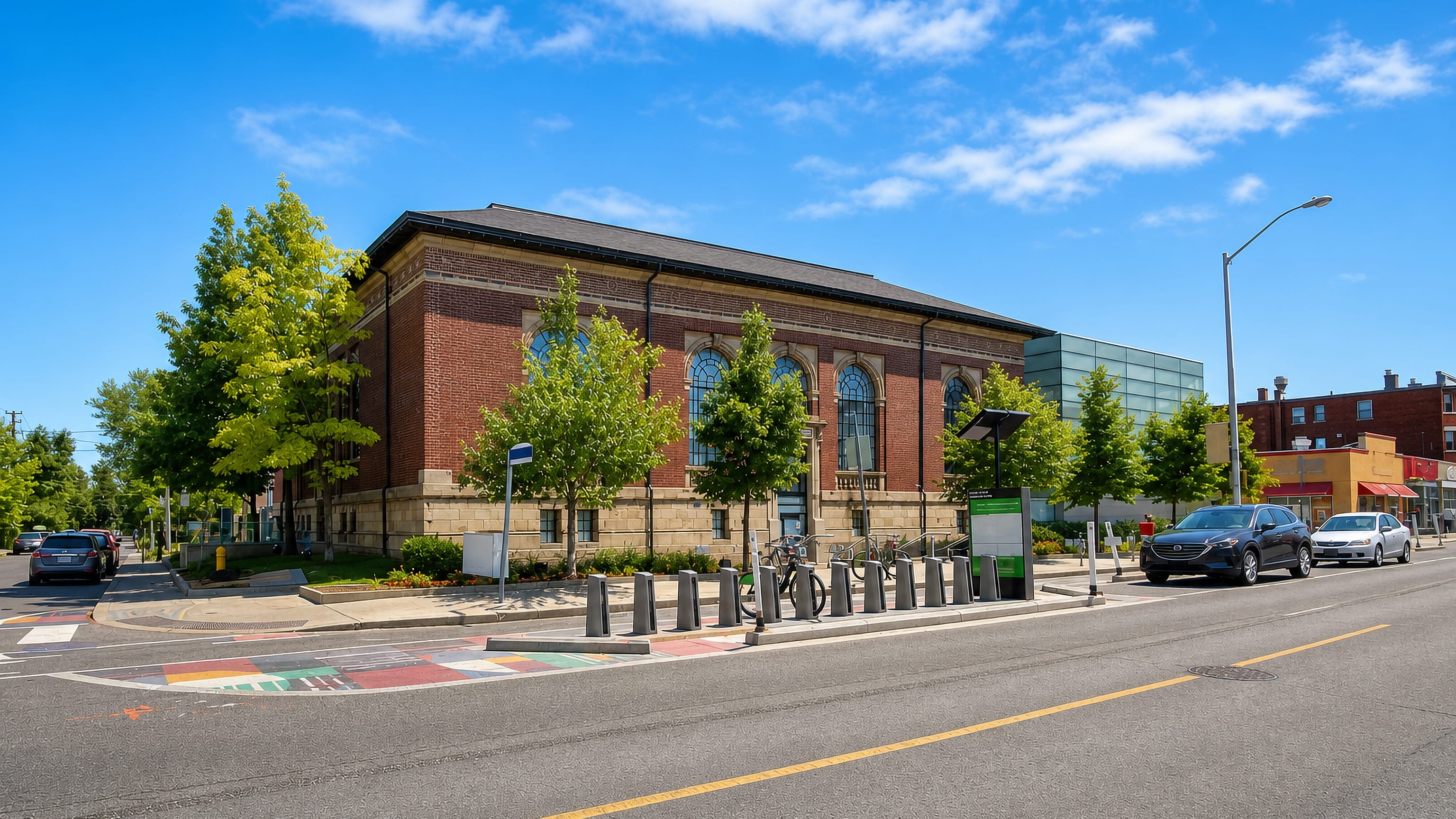 Red-brick civic building, street trees and bike-share docks on a corner in Dufferin Grove, Toronto.
