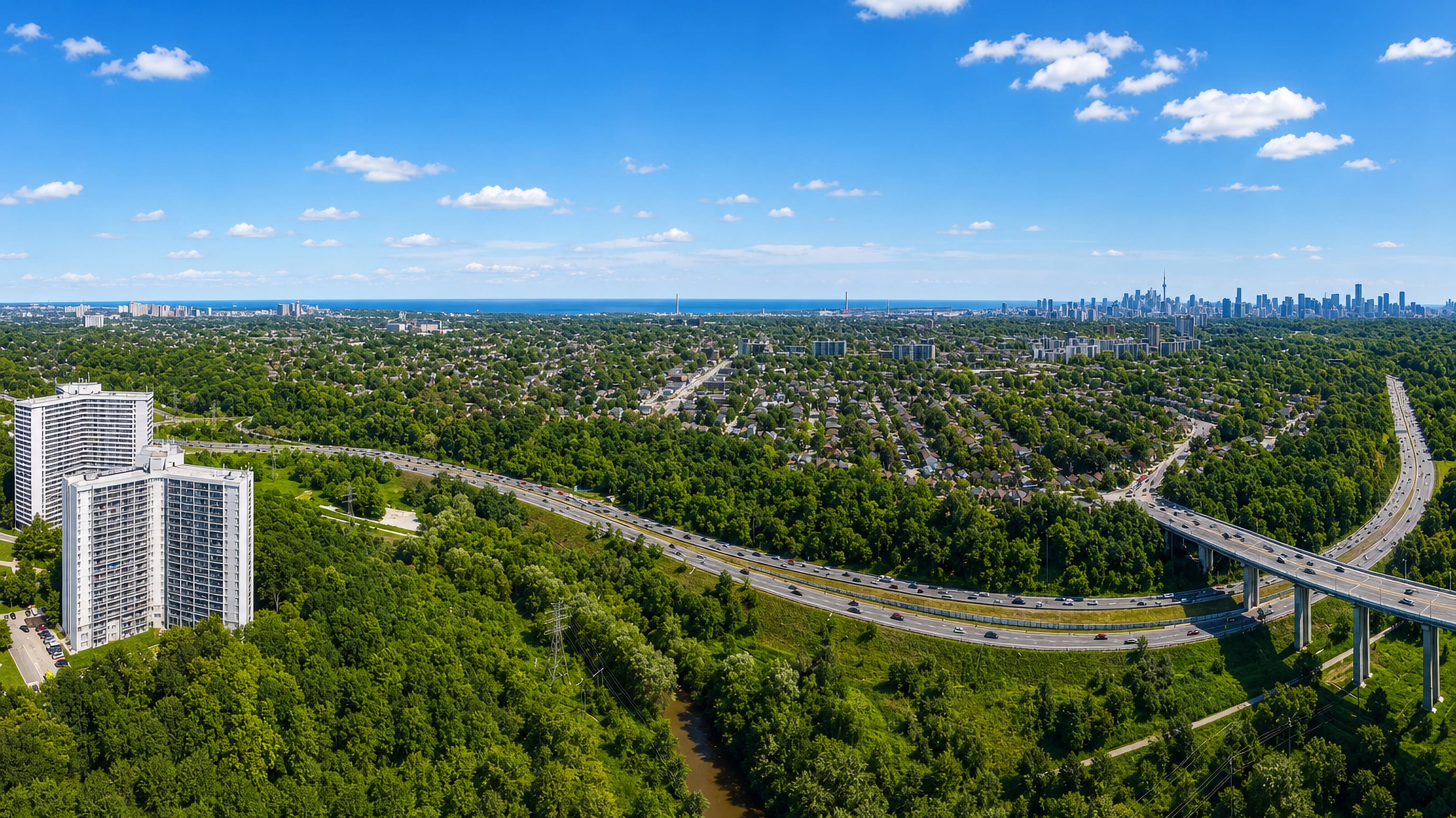 Aerial over East York's leafy streets and Don Valley ravine in Toronto, with the CN Tower on the horizon.