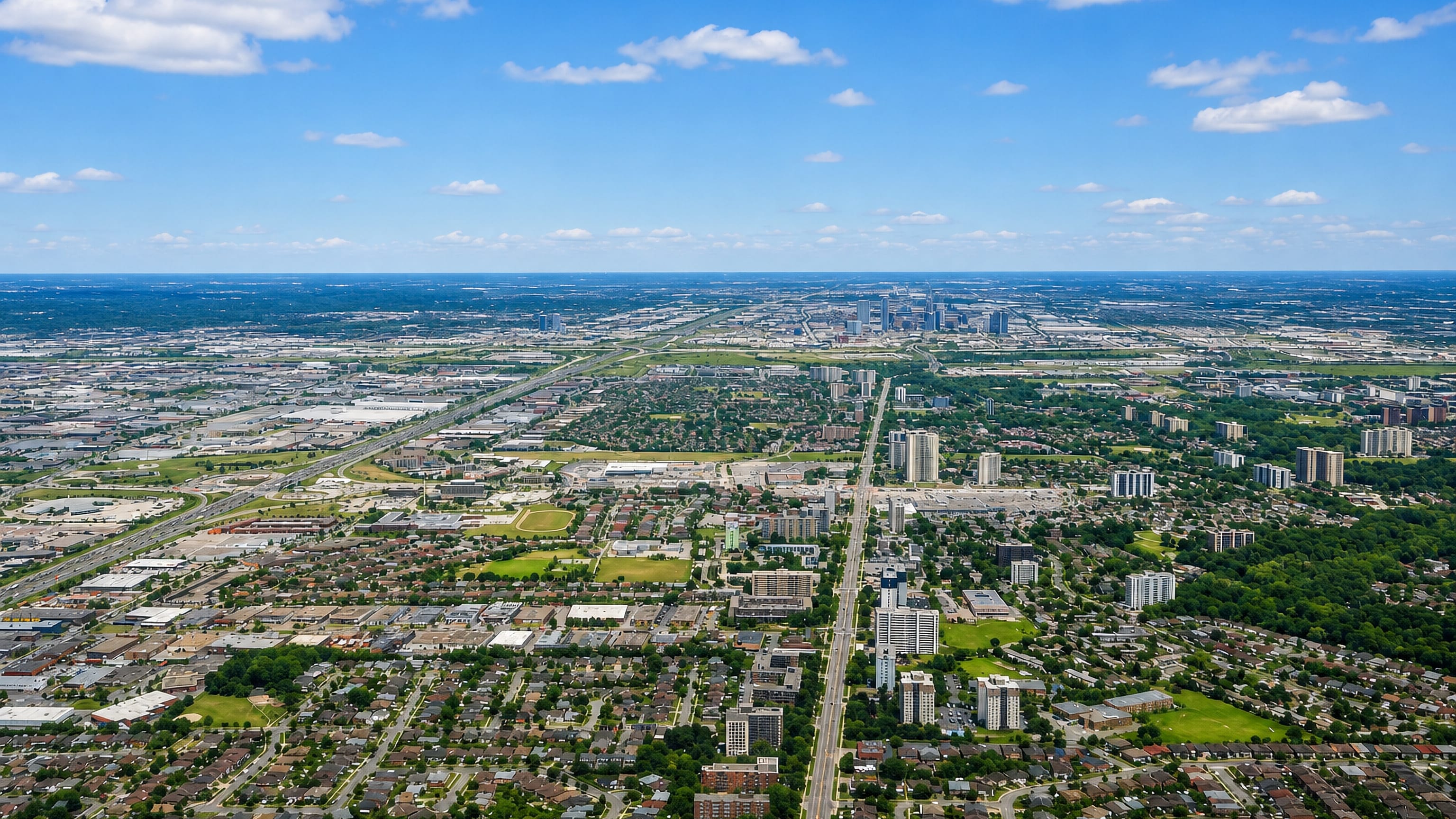Aerial over the Jane and Finch area of Toronto, apartment towers along the arterial with downtown beyond