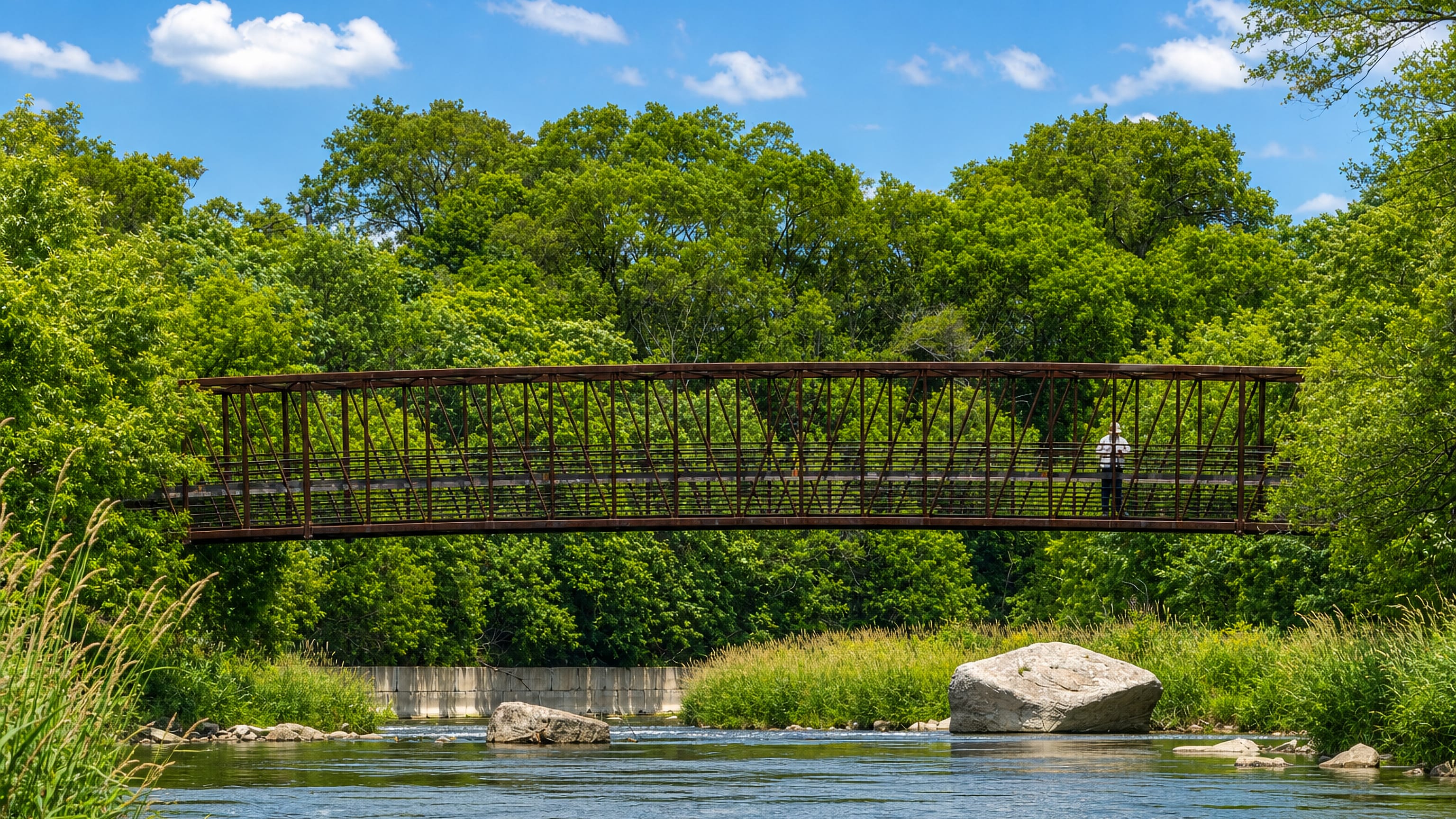 Steel pedestrian truss bridge over the Humber River amid summer greenery in Weston, Toronto.