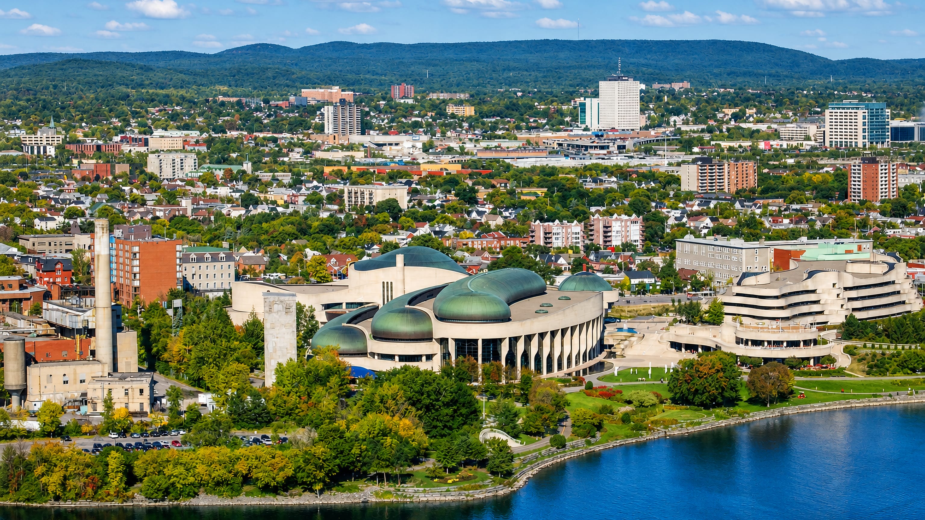 The Canadian Museum of History's domed wings on the Ottawa River shore, with Gatineau's skyline and hills beyond.