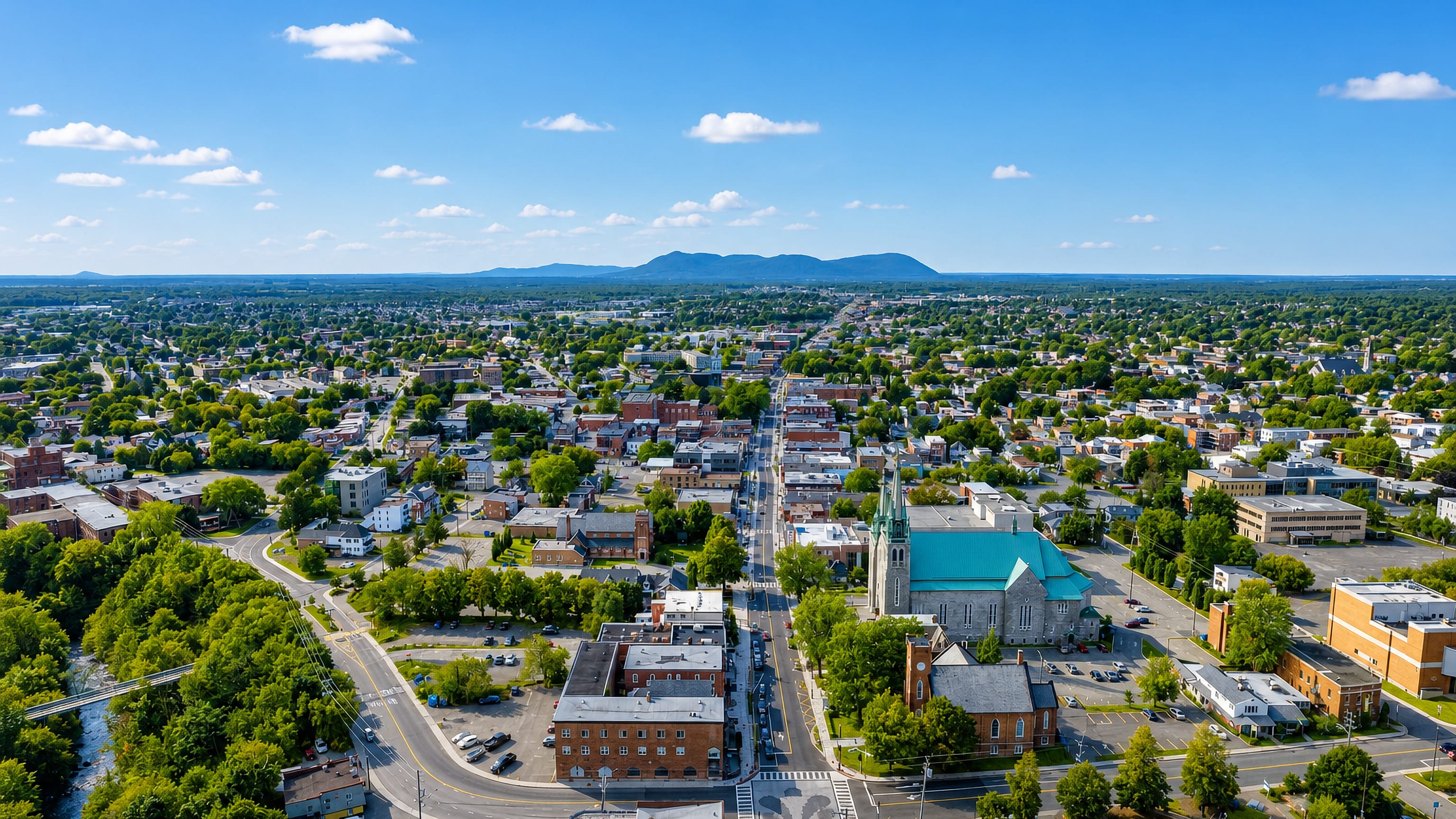 Aerial view along Granby's main street past its green-roofed church toward the Quebec countryside.