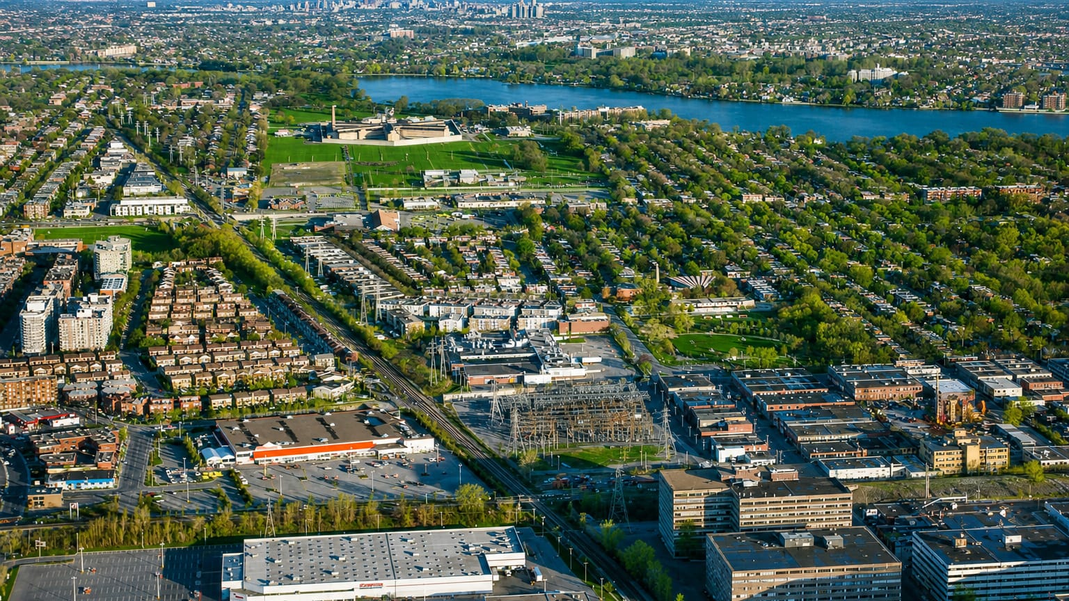 Aerial view over Ahuntsic-Cartierville's residential streets in Montreal, with the Riviere des Prairies and the distant downtown skyline.